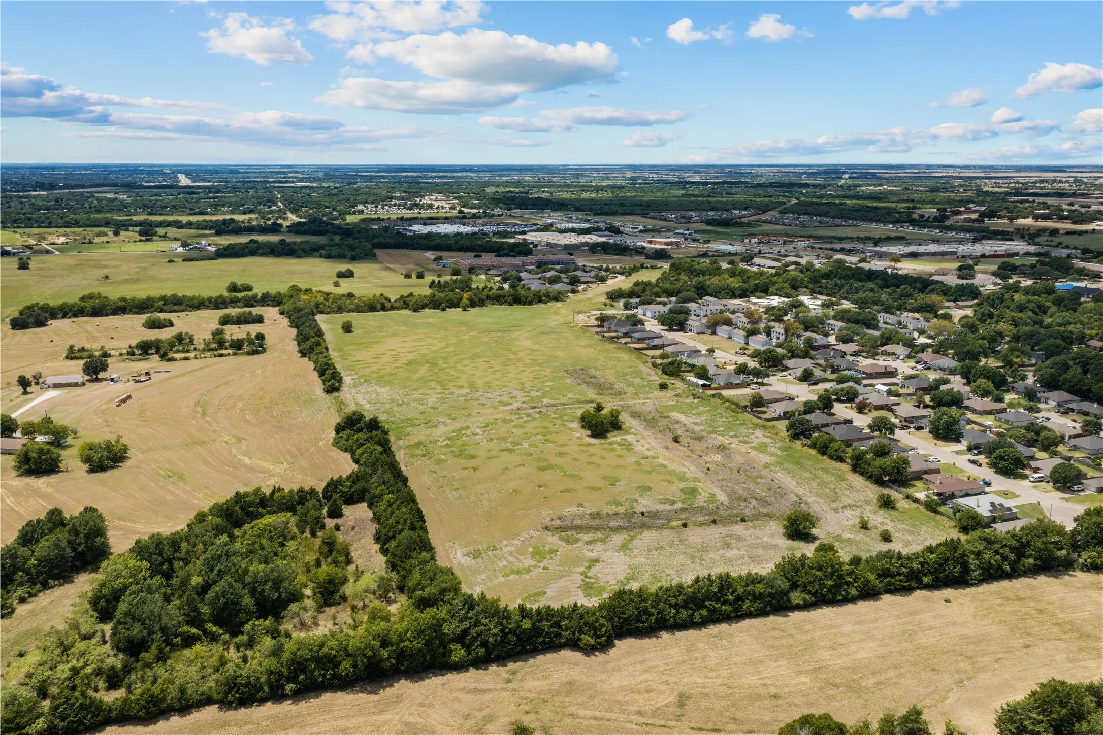 Expansive parcel of land with varied terrain, featuring open fields and treed borders