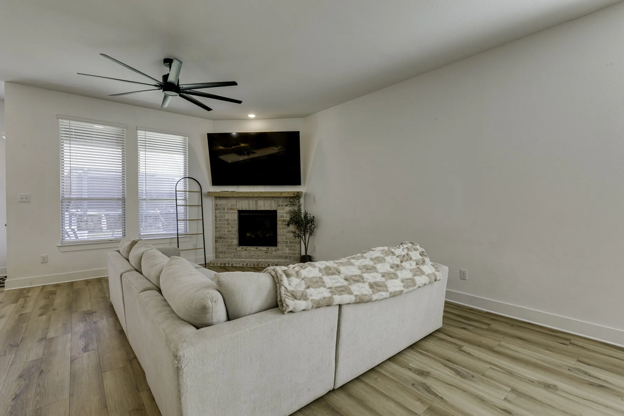 Corner fireplace with brick surround, wood-finish flooring, and a ceiling fan