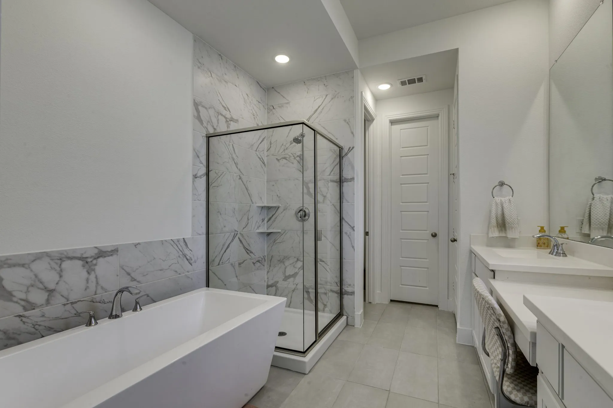 Freestanding soaking tub, glass-enclosed shower with tile surround, dual vanity with undermount sinks, and built-in vanity seating