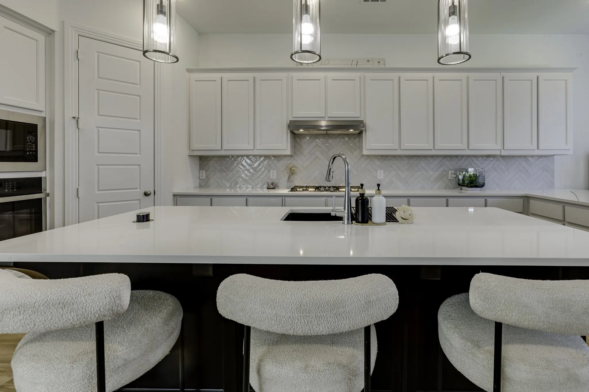Kitchen featuring a large central island, stainless steel appliances, a herringbone tile backsplash, pendant lighting, and abundant cabinetry. The island, has seating for 3+, and be sure to notice the island pop-up electrical outlet left of the sink.