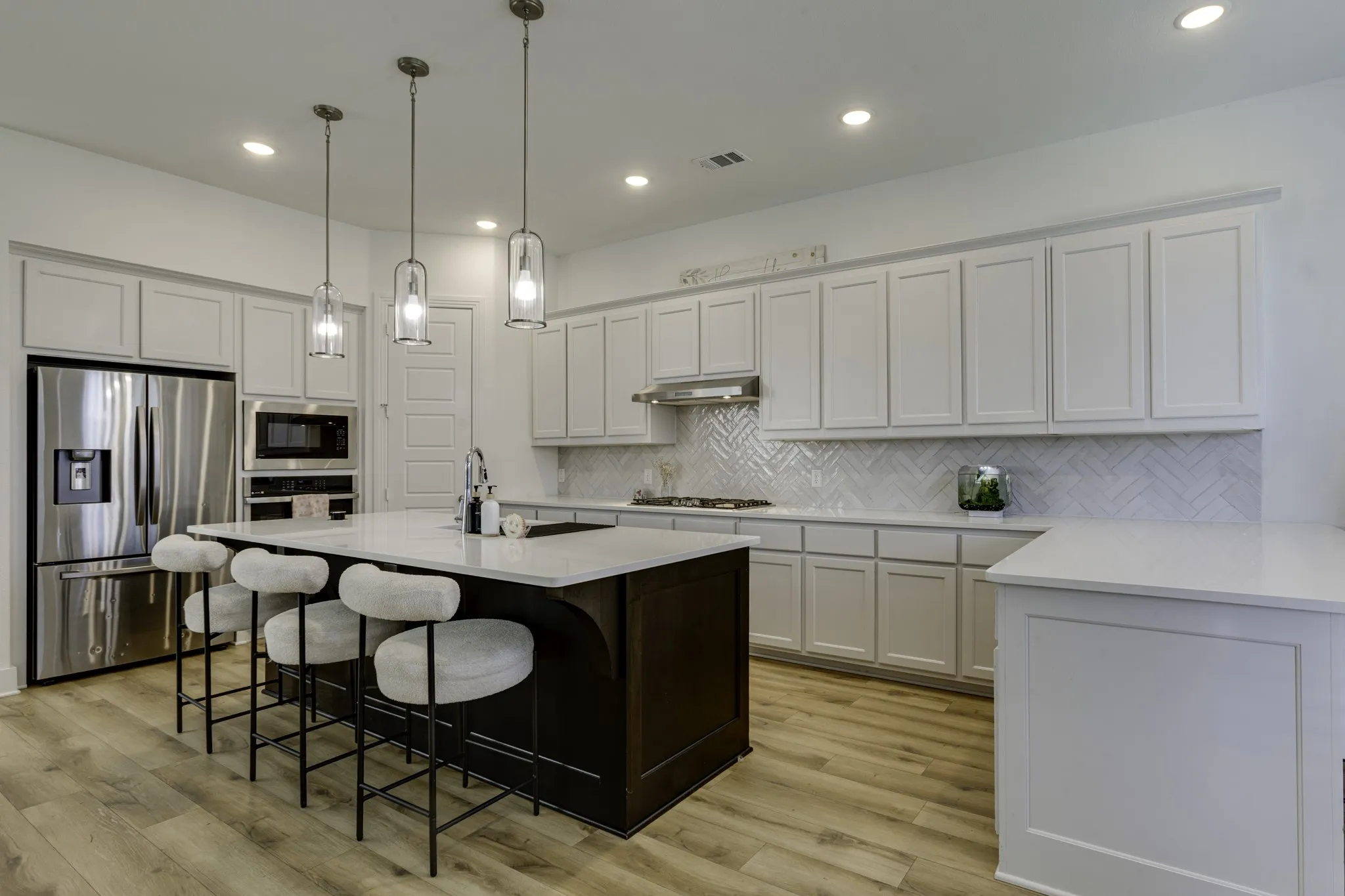 Kitchen featuring a dark-toned island with a light-toned countertop, stainless steel appliances, white cabinetry, a herringbone tile backsplash, and wood-finish flooring