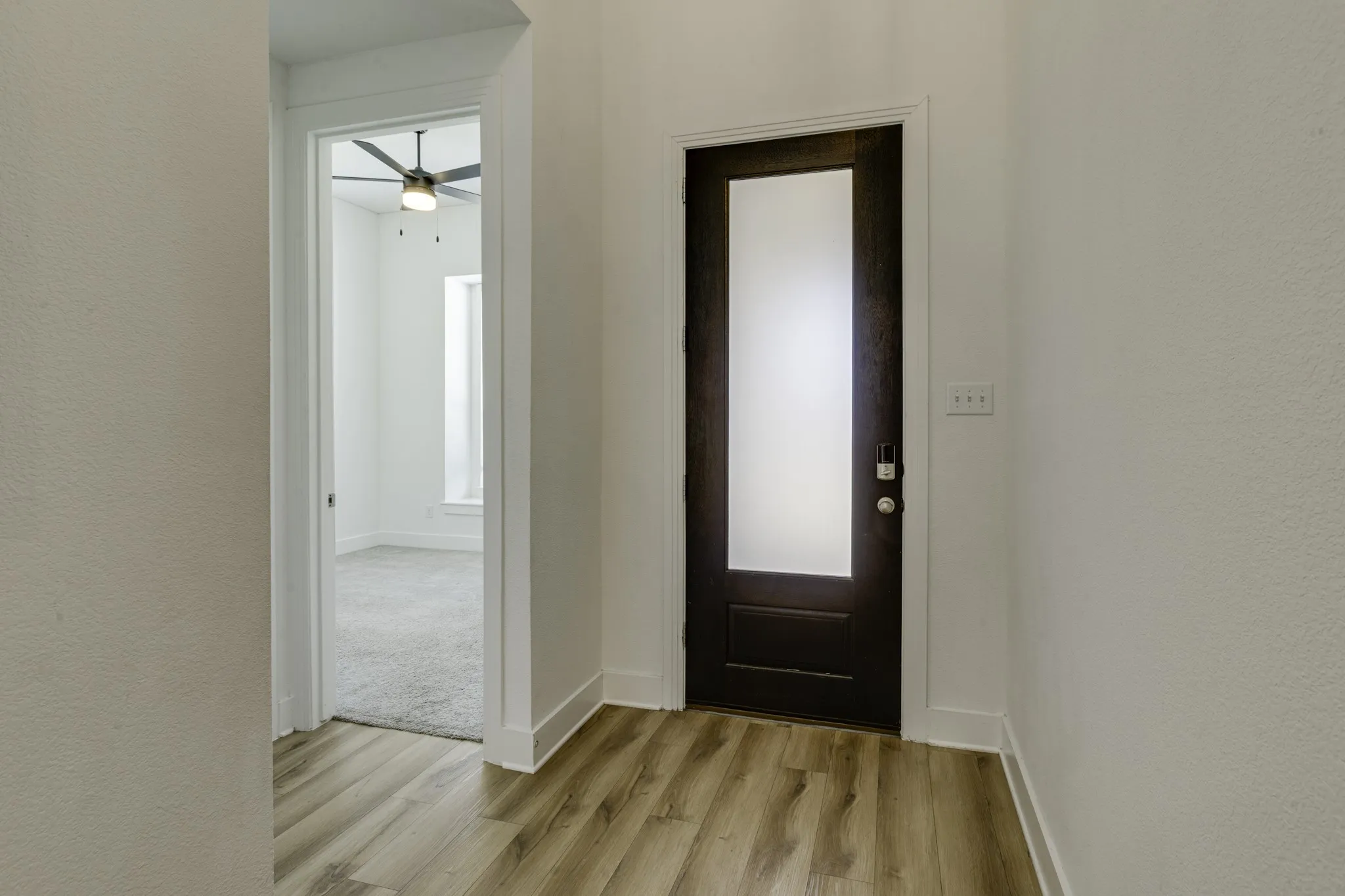 Wood-finish flooring leading to a dark wood-paneled door with frosted glass