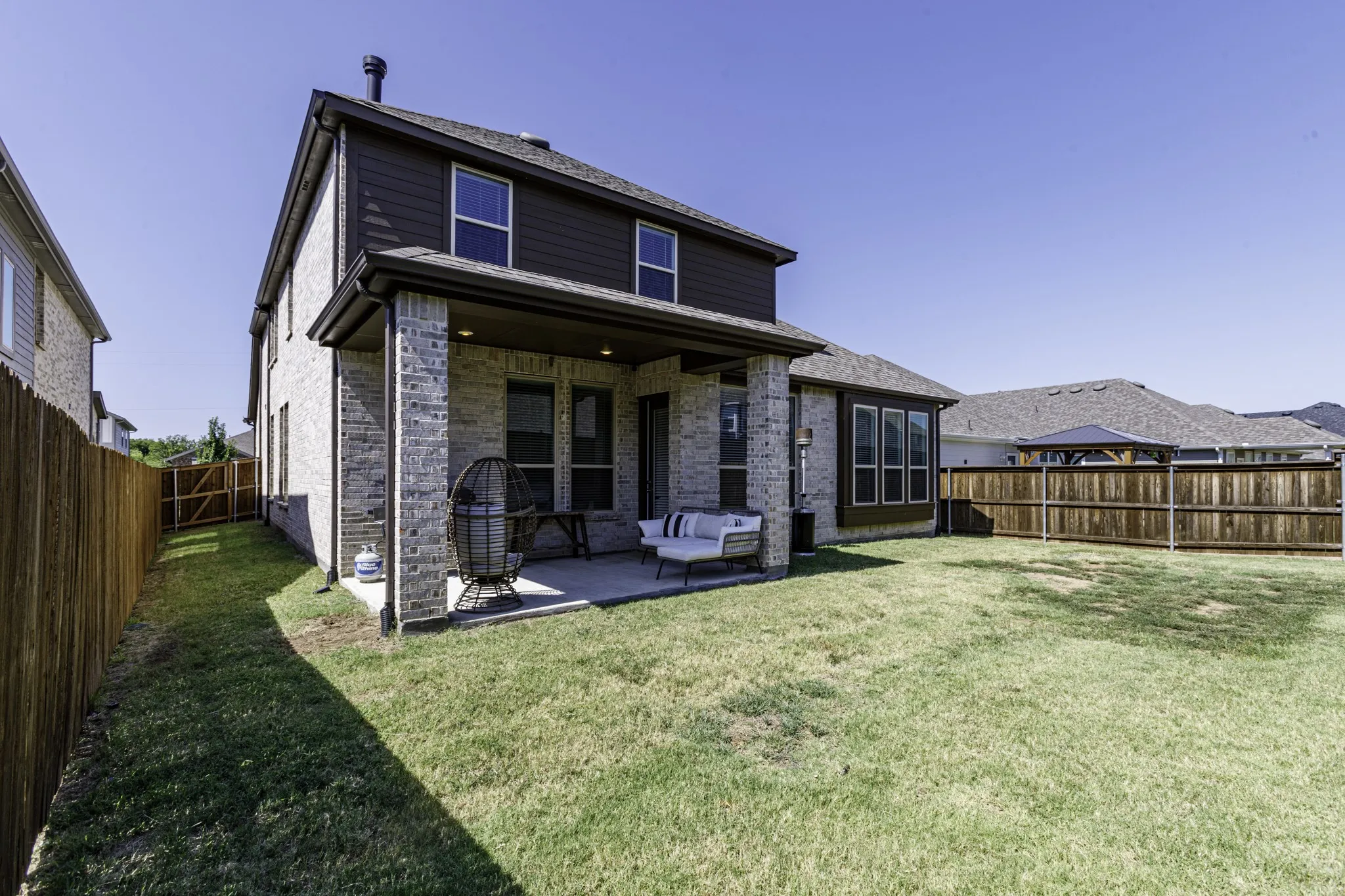 Expansive backyard featuring a covered patio, brick and siding exterior, large windows, and a wood privacy fence