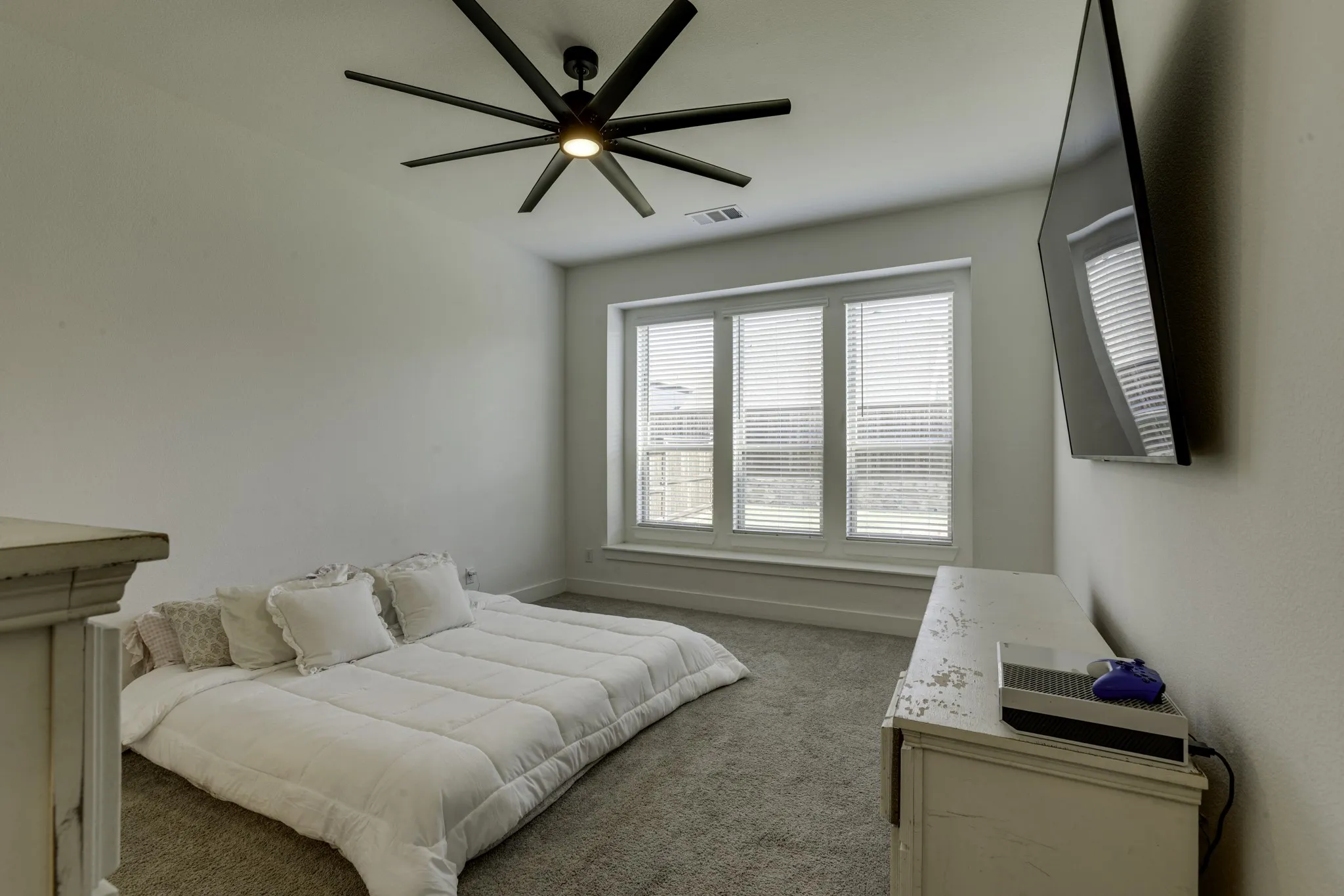 The master bedroom features recessed lighting, ceiling fan with integrated light, multiple windows with blinds, wall-mounted display, and carpeted flooring