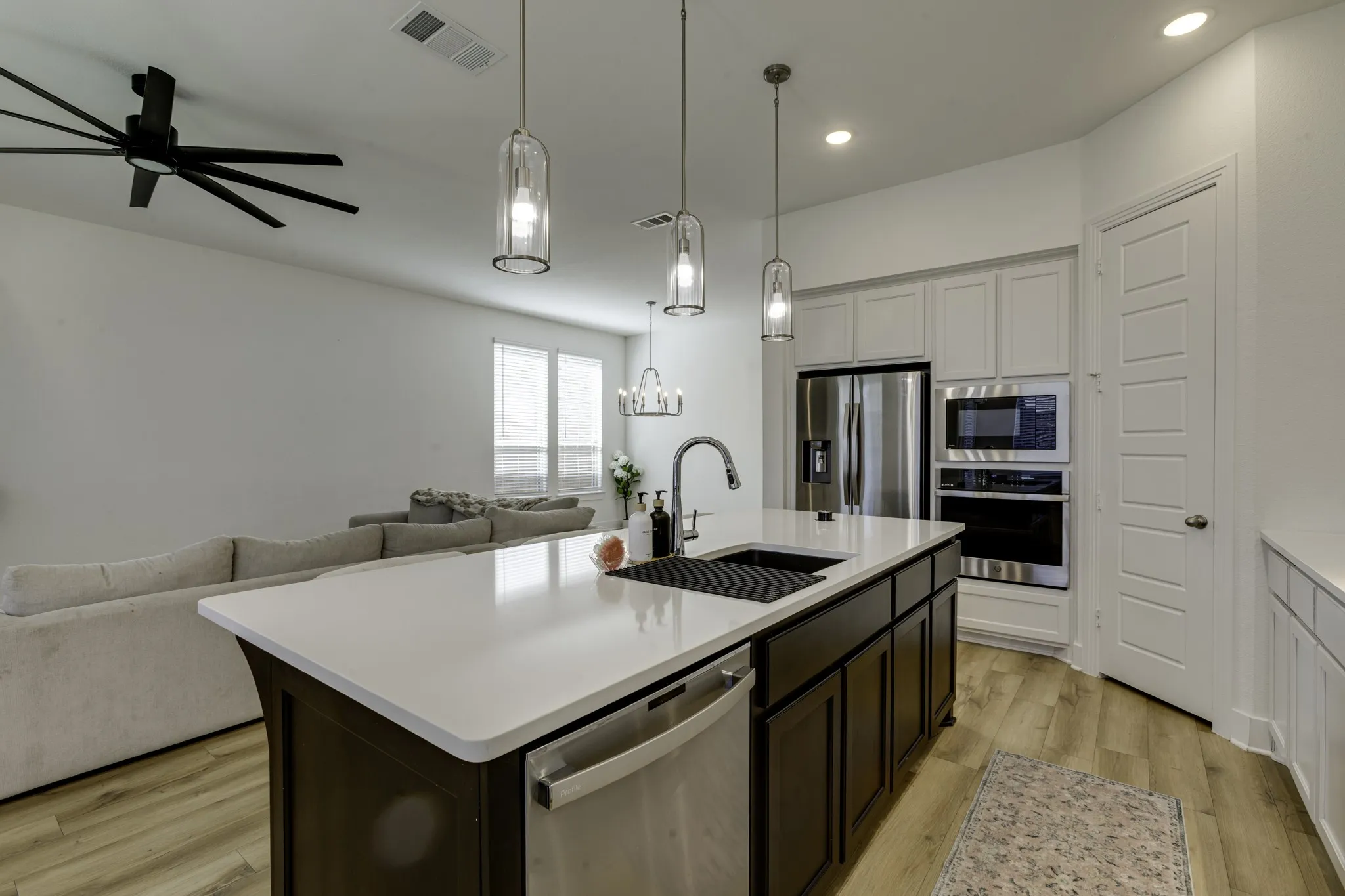 Kitchen island with a white countertop and dark cabinetry, featuring a built-in sink and stainless steel dishwasher