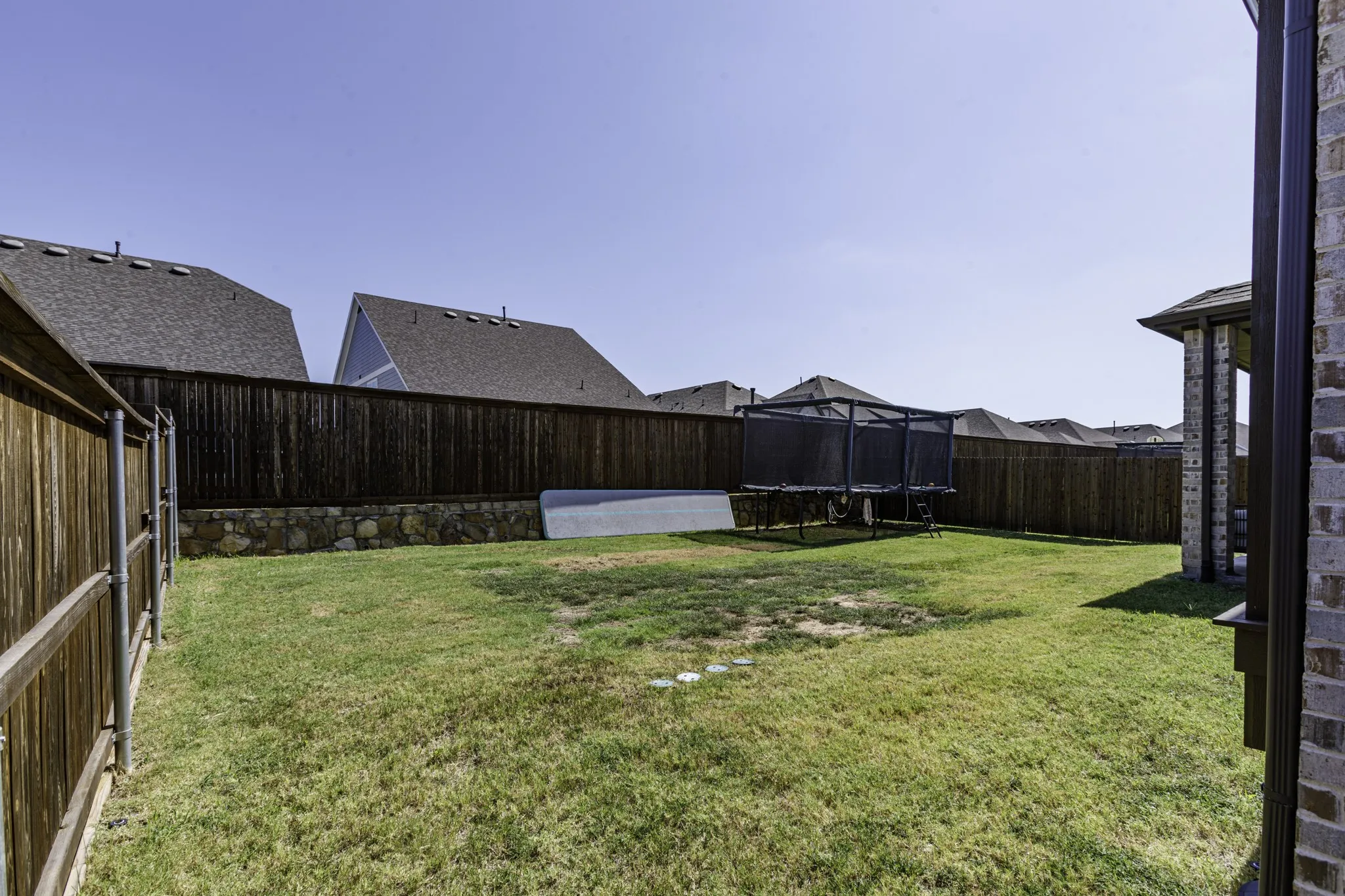 Expansive backyard featuring a manicured lawn, full wood fencing, and a stone retaining wall