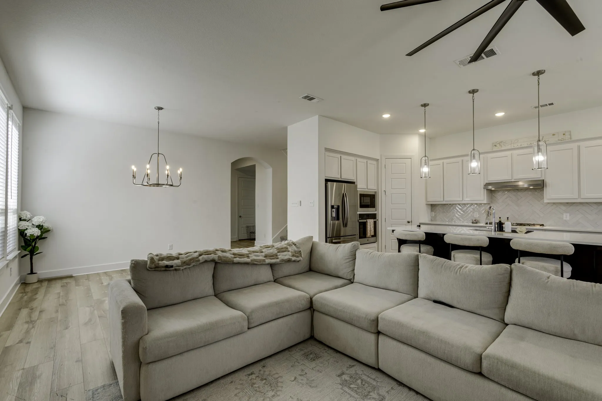Open-concept living area featuring wood-finish flooring, a contemporary chandelier, and a ceiling fan.