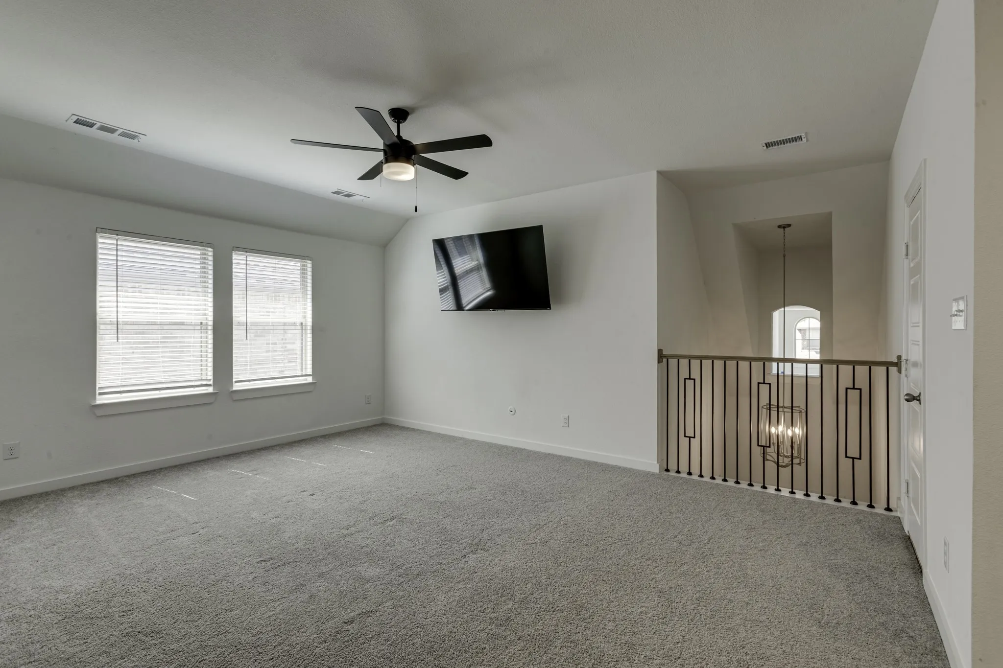 Upstairs gameroom, with carpeted room featuring a vaulted ceiling with a ceiling fan, dual windows with blinds, and a built-in television mount