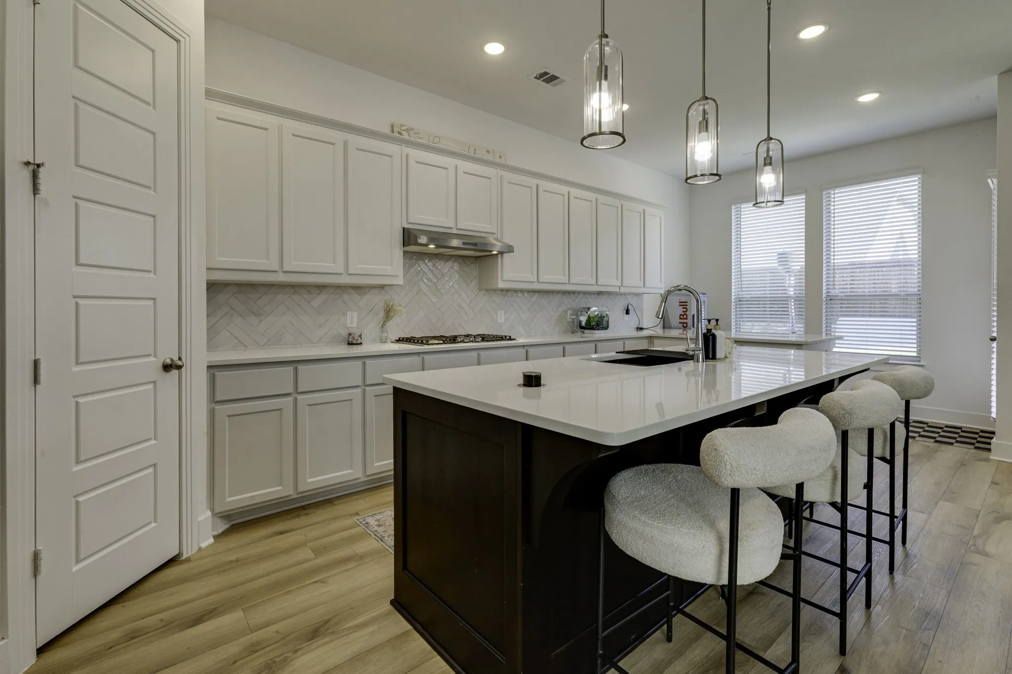 Kitchen featuring wood-finish flooring, white cabinetry, a herringbone tile backsplash, and a central island with a built-in sink and pendant lighting