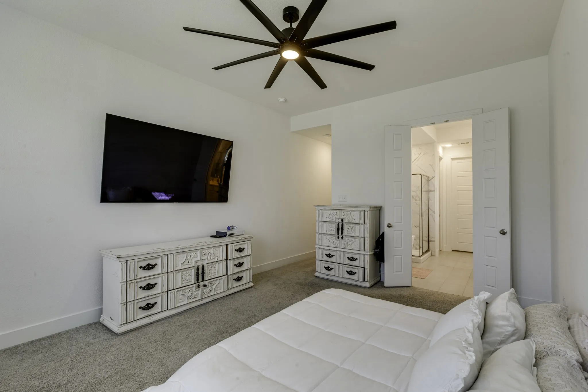 The master bedroom has carpeted flooring, contemporary ceiling fan, built-in wall-mounted television, double-door entry, and a tiled shower with glass enclosure