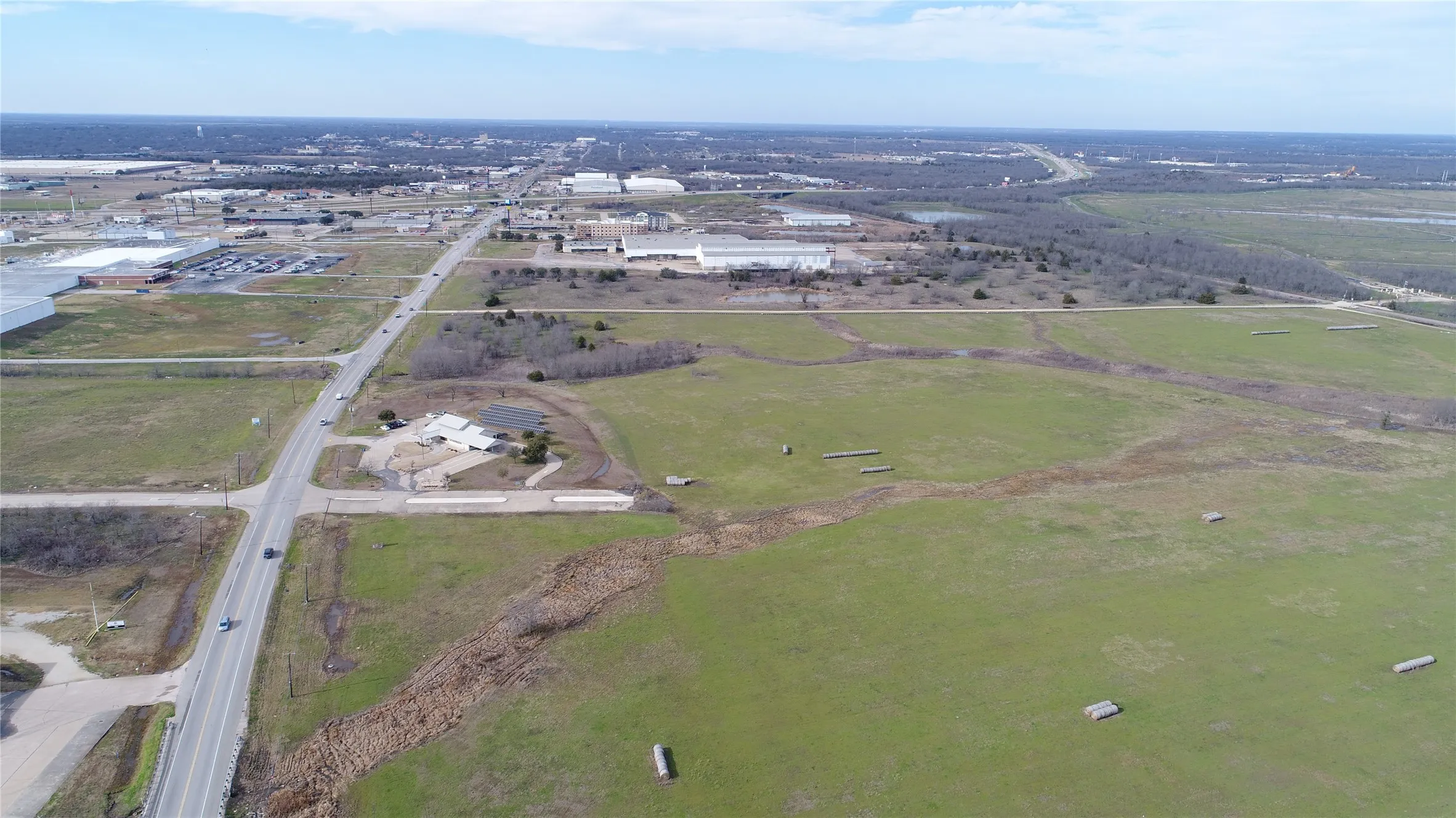 Expansive green fields with scattered trees, bordered by a paved road