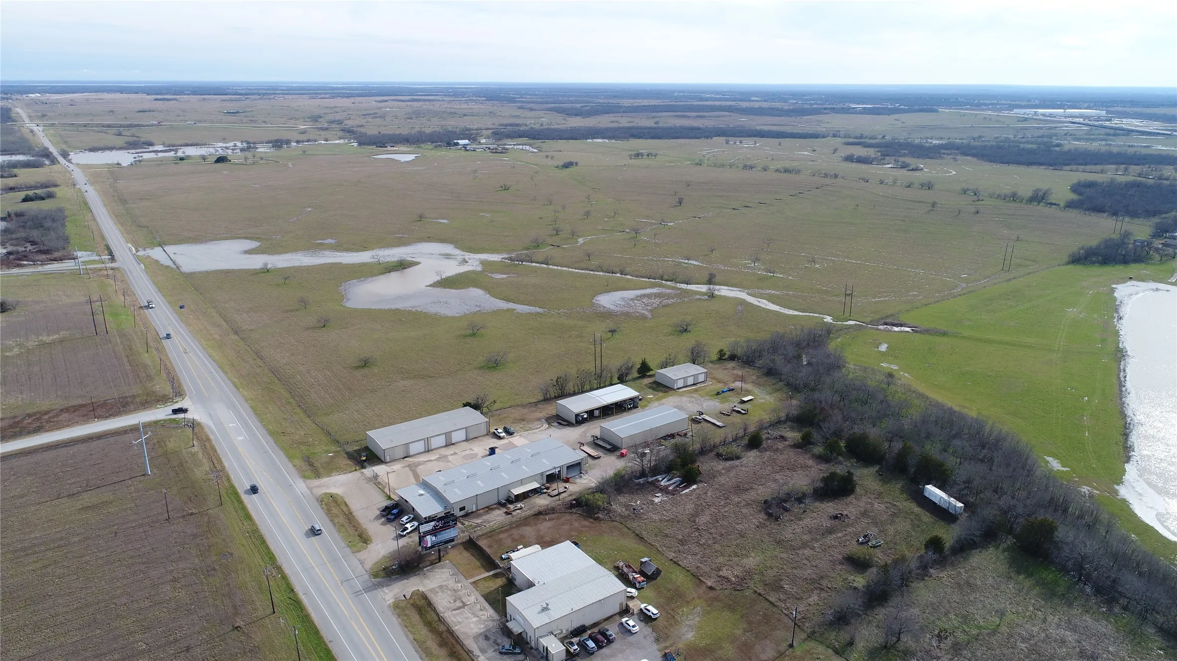 Expansive acreage featuring multiple industrial buildings, a paved roadway, and open fields