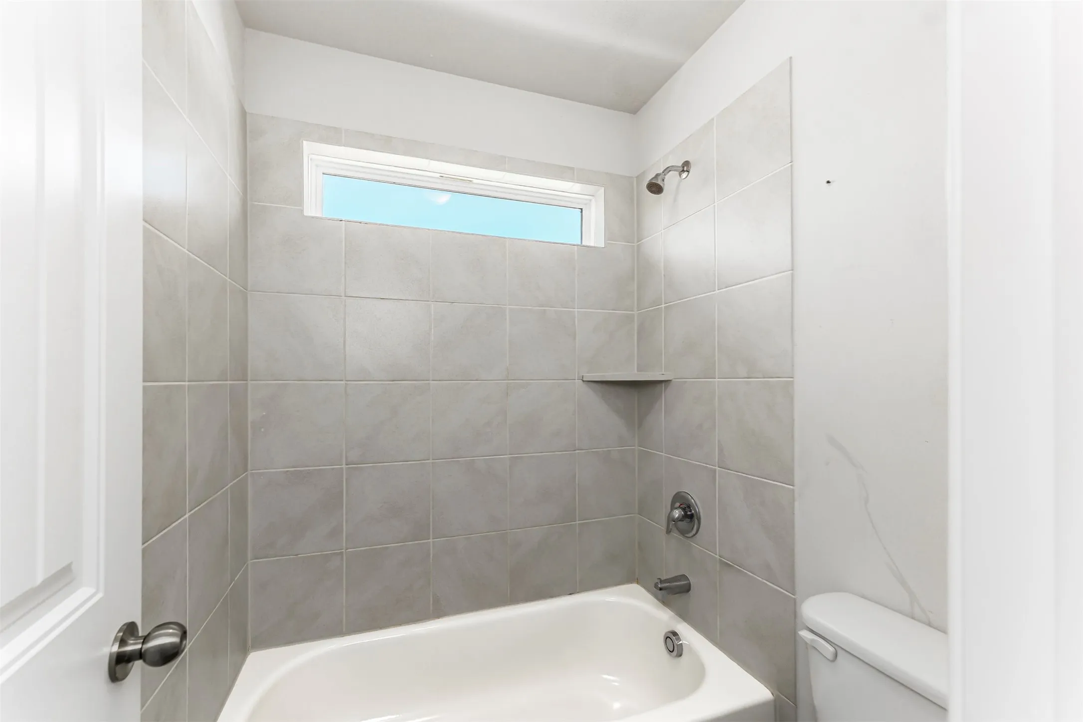 Bathtub with a tiled surround, integrated shower, and a built-in shelf