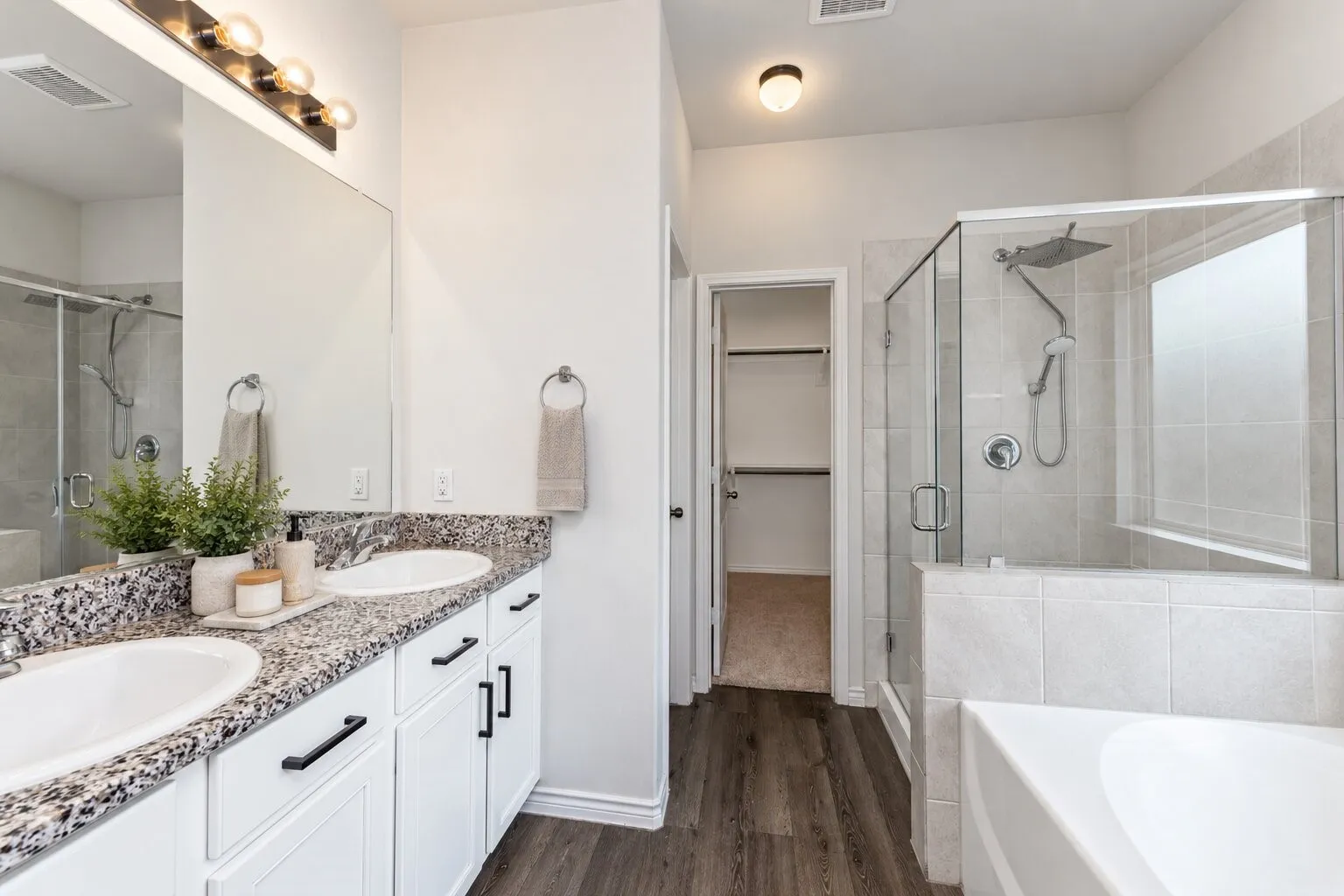 *virtually staged* Dual vanity with speckled countertop and white cabinetry, glass-enclosed shower with tiled walls, built-in bathtub, and wood-finish flooring