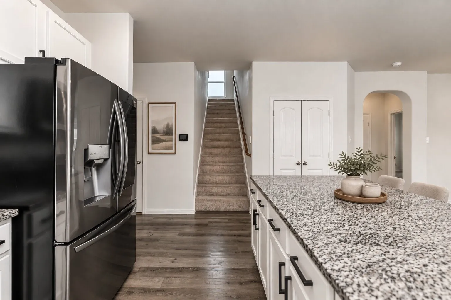 *virtually staged* Stainless steel refrigerator, white cabinetry with black hardware, wood-finish flooring, and a stone countertop