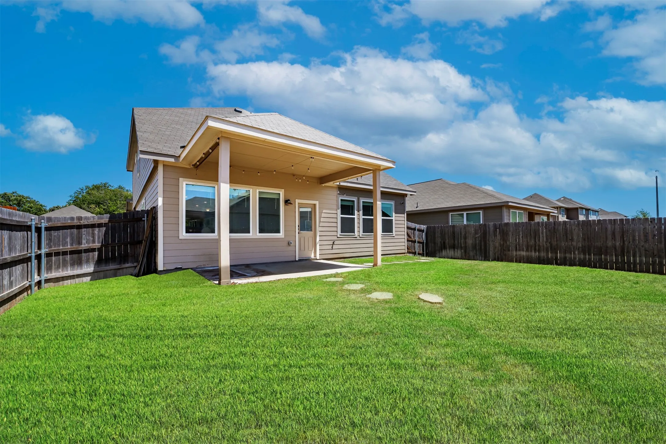 Expansive grass lawn with a covered patio, privacy fencing, and stone pavers