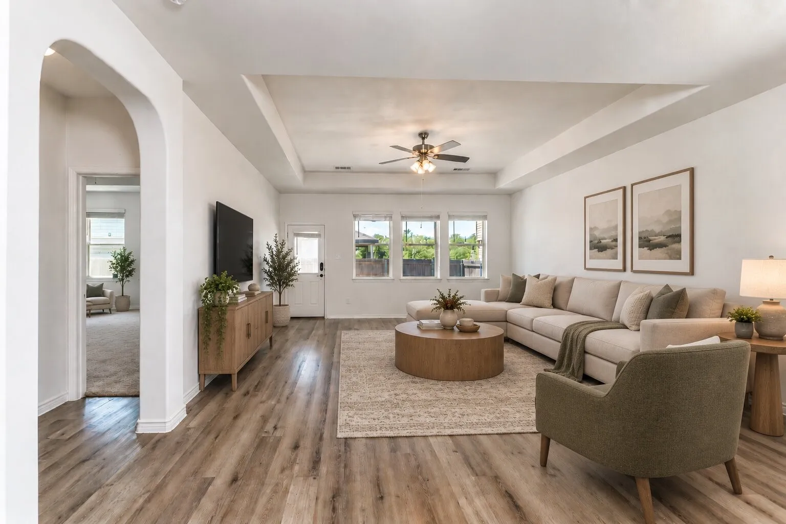 *virtually staged* Spacious living area featuring wood-finish flooring, a tray ceiling with a ceiling fan, multiple windows, and an arched entryway