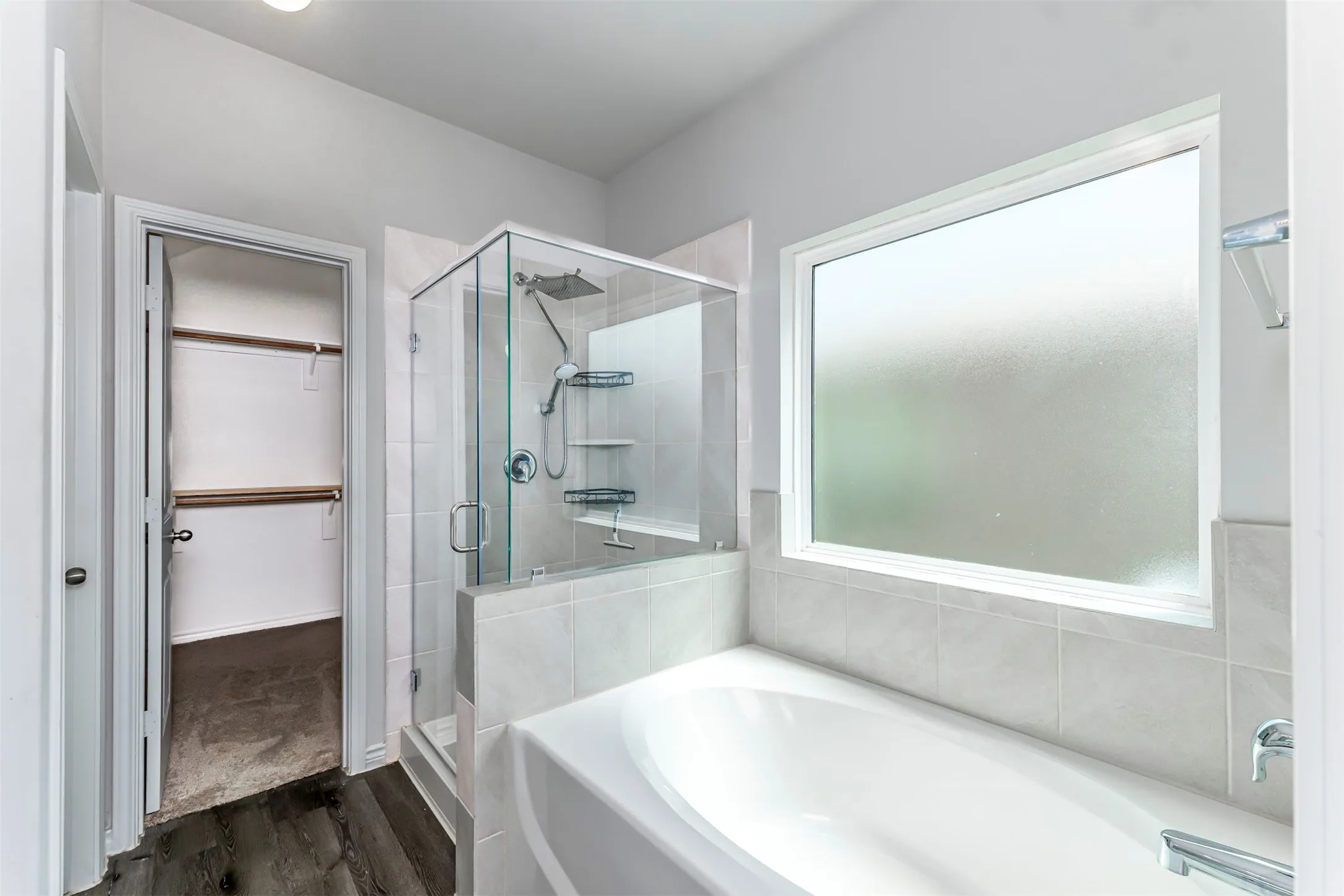 Soaking tub with a tiled surround, glass-enclosed shower, and a large frosted window