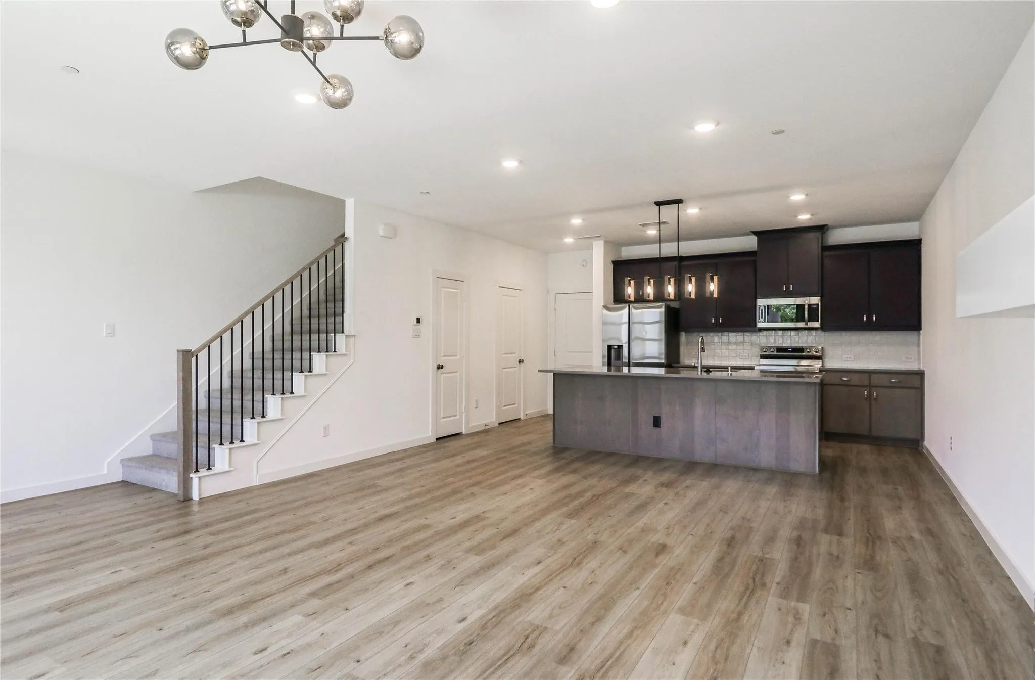 Kitchen featuring appliances with stainless steel finishes, tasteful backsplash, light wood finished floors, a kitchen island with sink, and hanging light fixtures