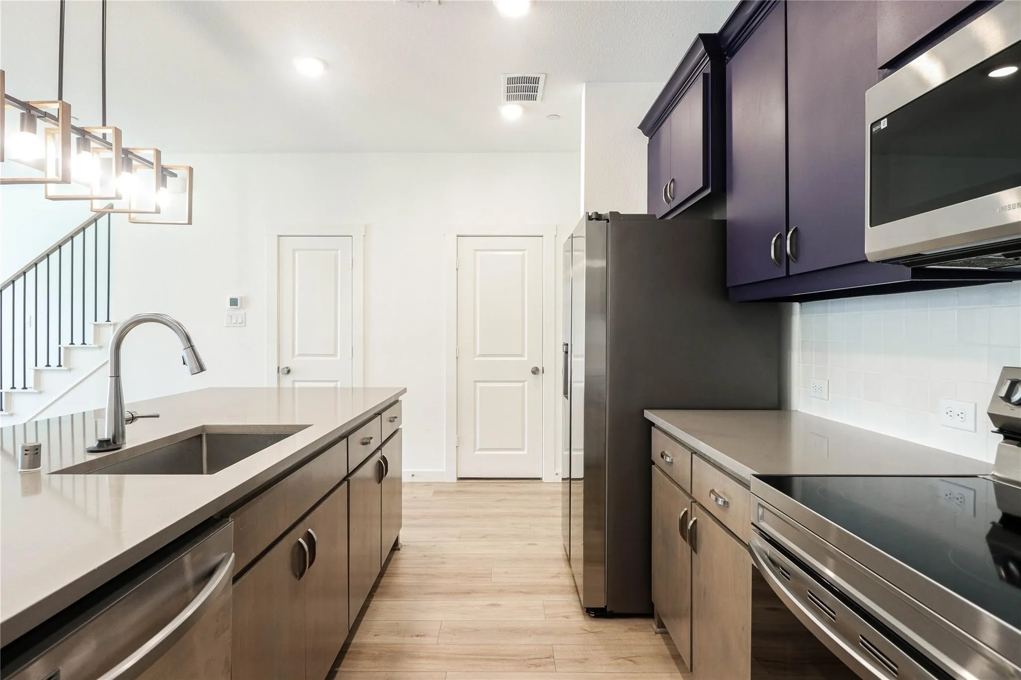 Kitchen featuring stainless steel appliances, light wood-type flooring, tasteful backsplash, light countertops, and pendant lighting
