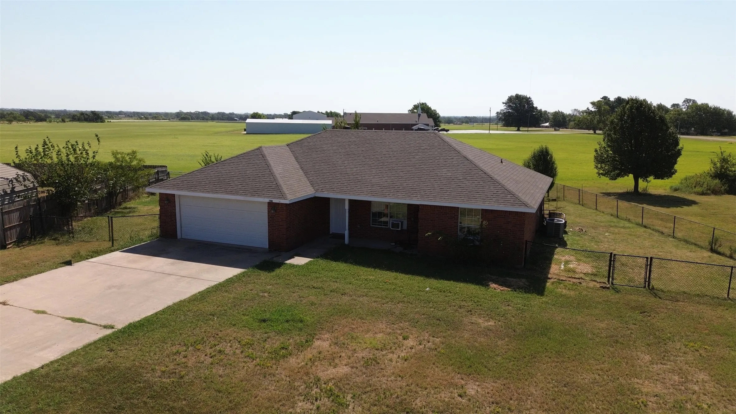 Brick exterior with an attached garage, paved driveway, and fenced perimeter