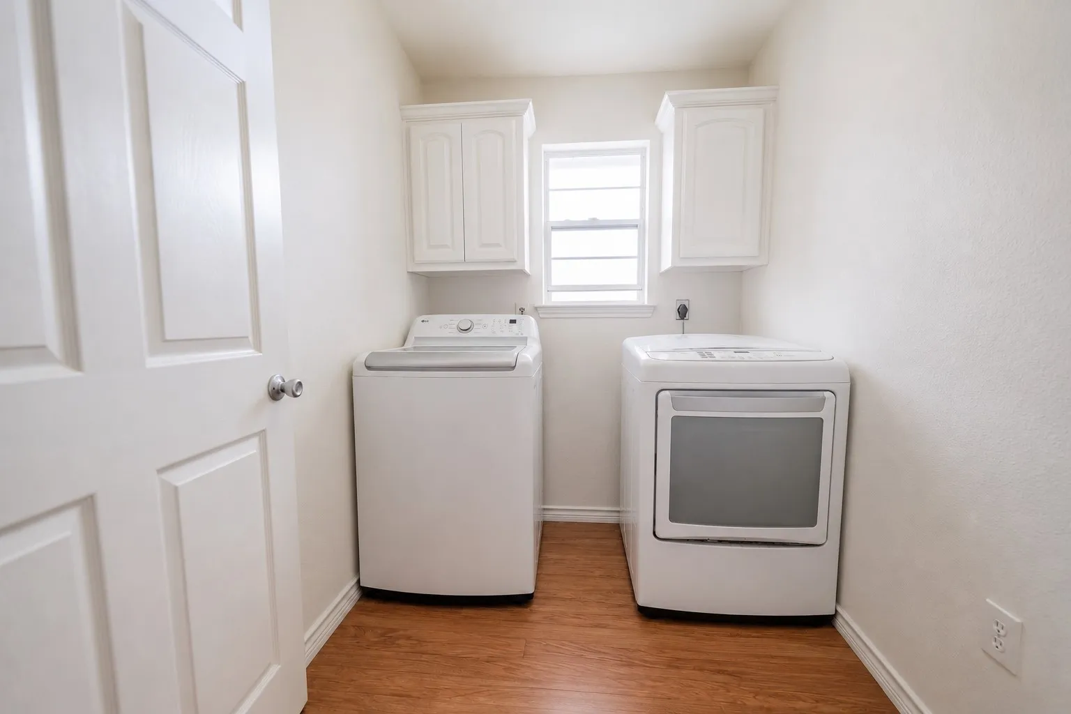 Dedicated utility space featuring wood-finish flooring, white paneled door, and built-in white cabinetry