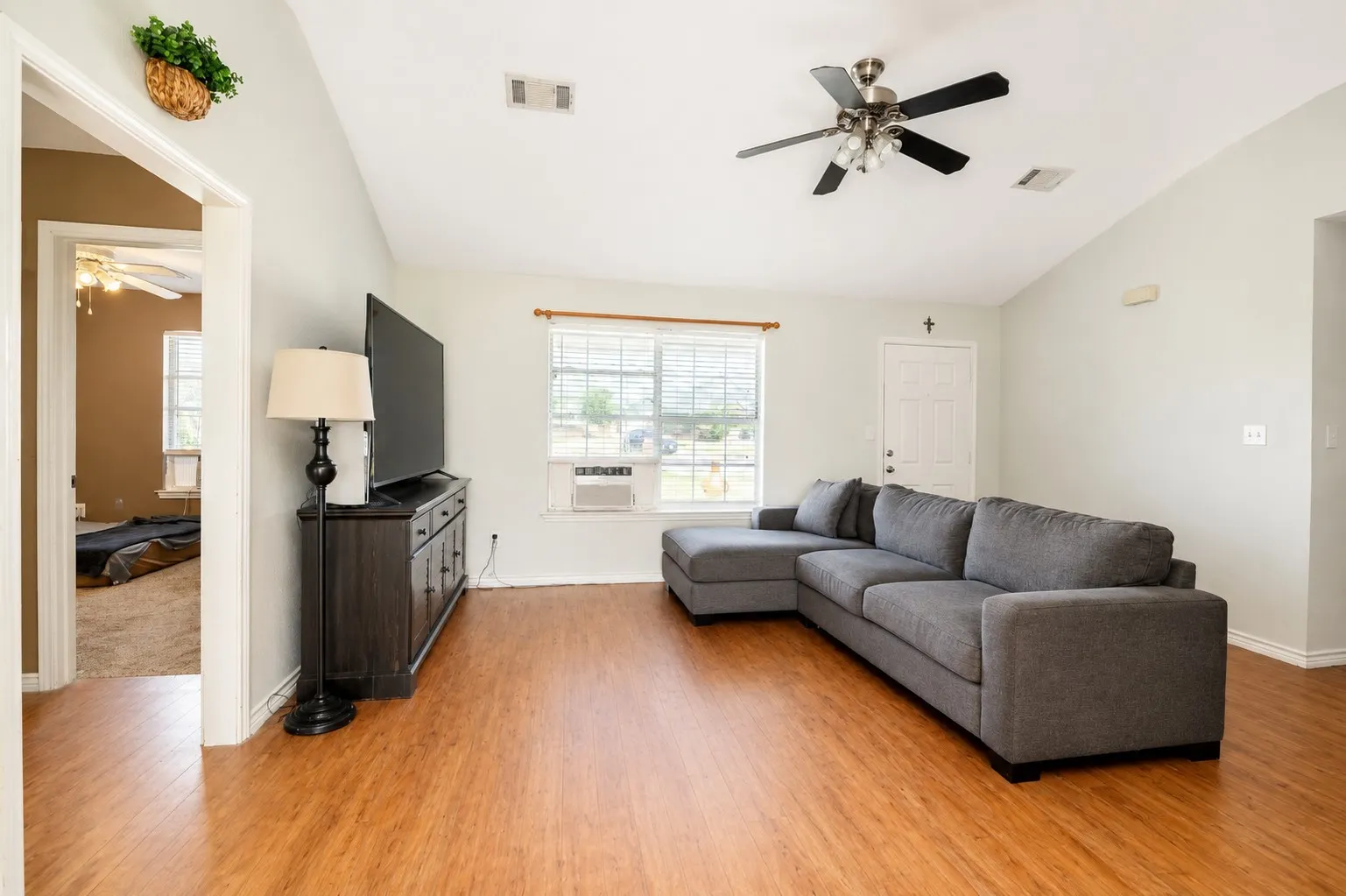 Vaulted ceiling living area featuring wood-finish flooring, a ceiling fan, and multiple windows