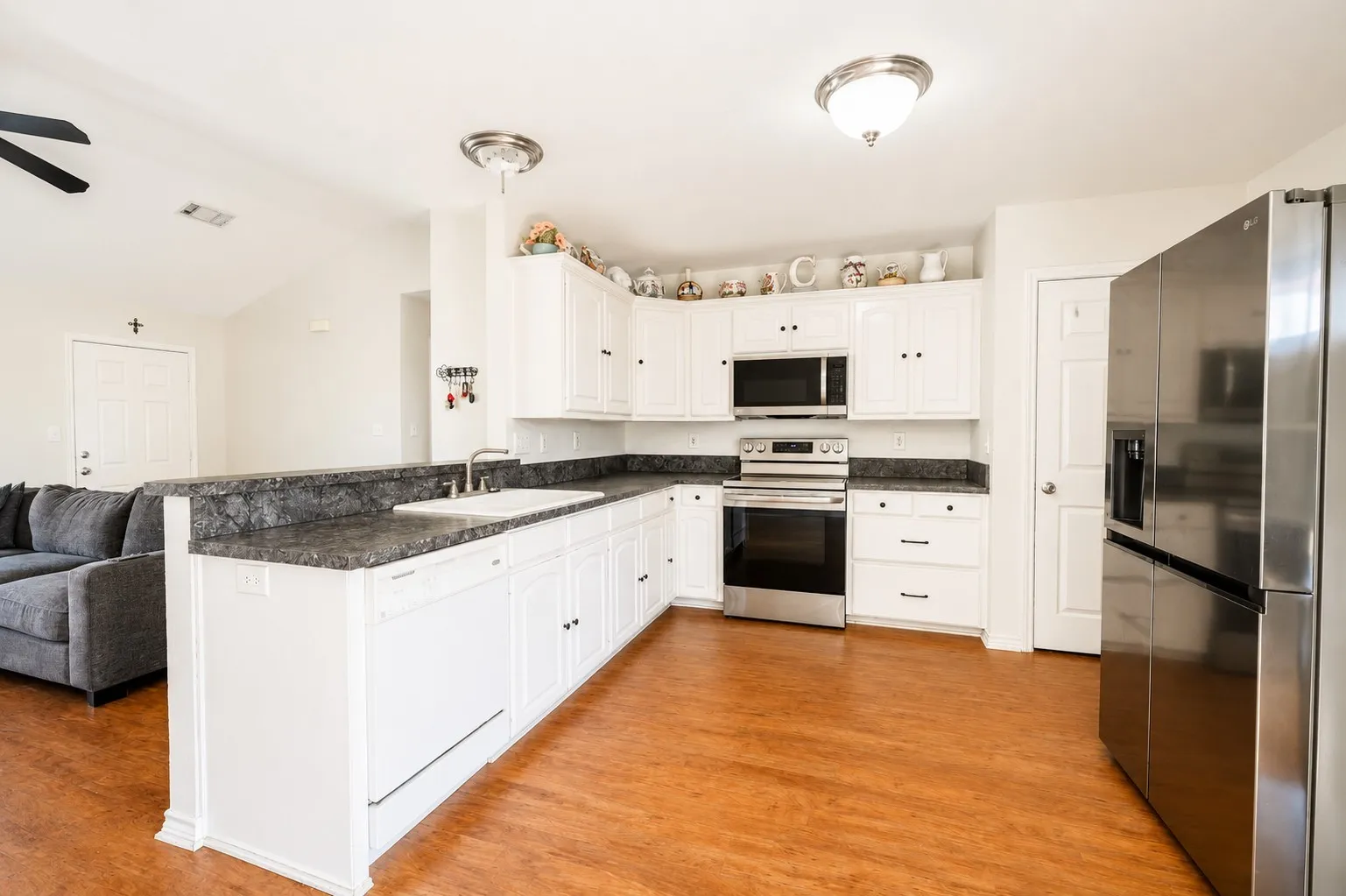 Kitchen featuring white cabinetry, dark countertops, stainless steel appliances, and wood-finish flooring