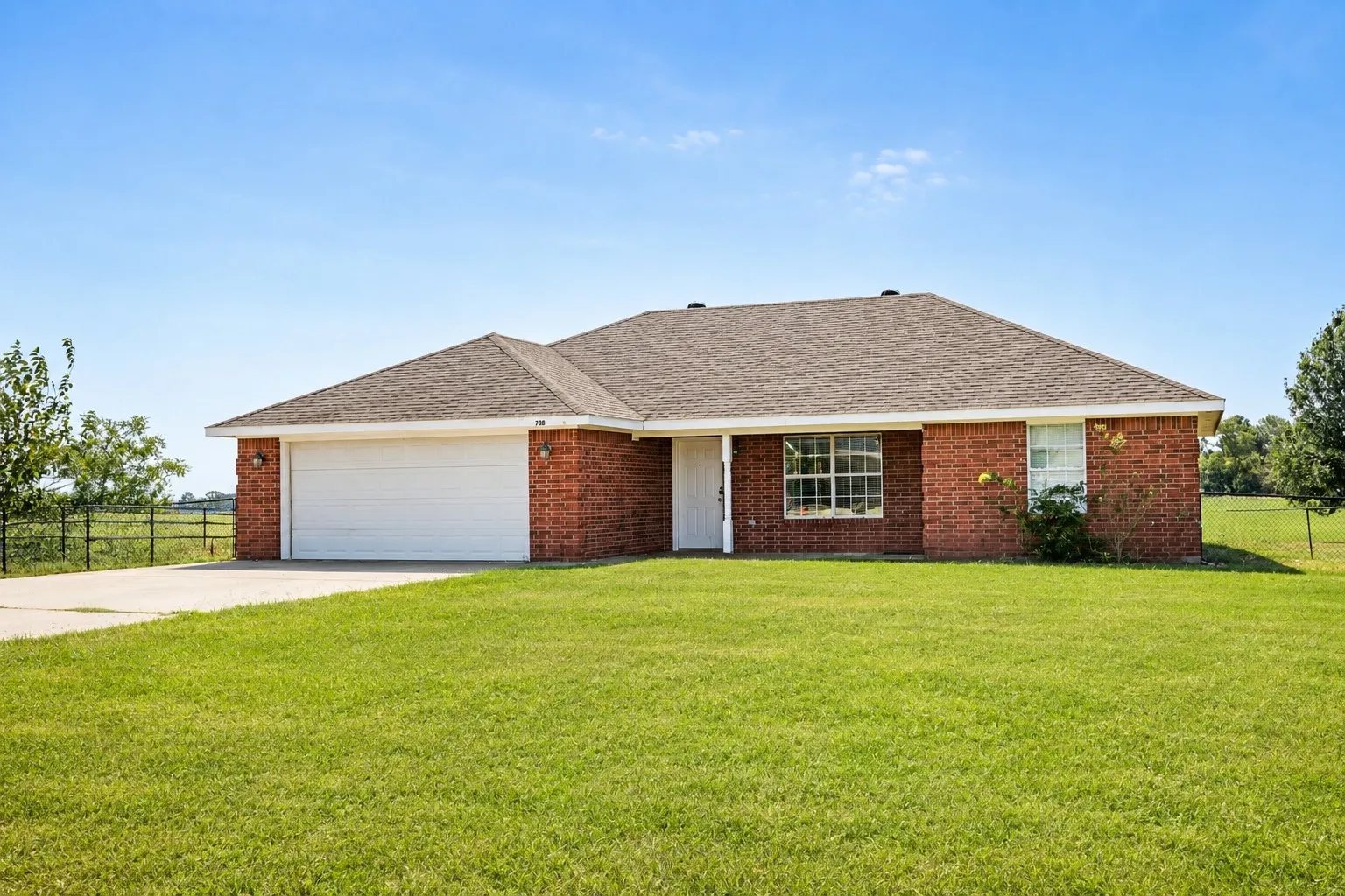 Red brick exterior, attached garage, concrete driveway, front yard with green lawn, and a light-colored shingle roof