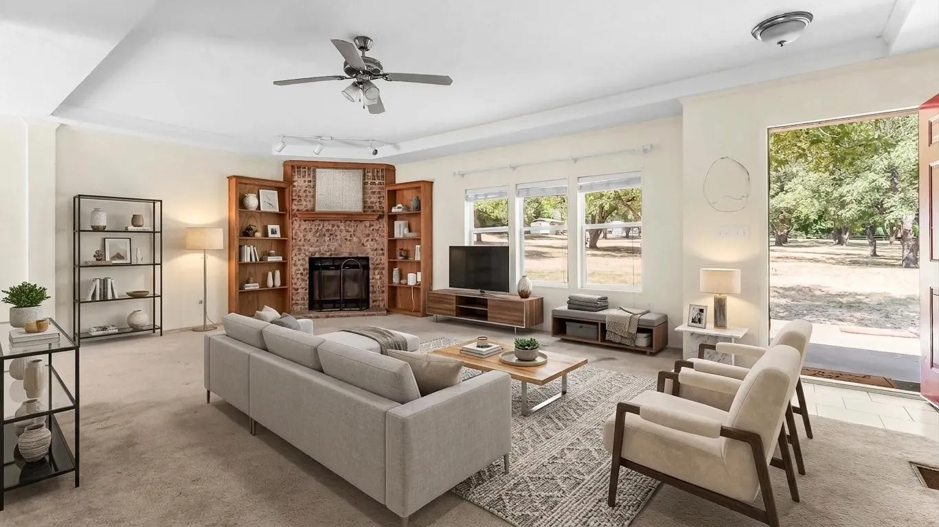 Living area featuring a brick fireplace surround, built-in shelving, a ceiling fan, and multiple windows