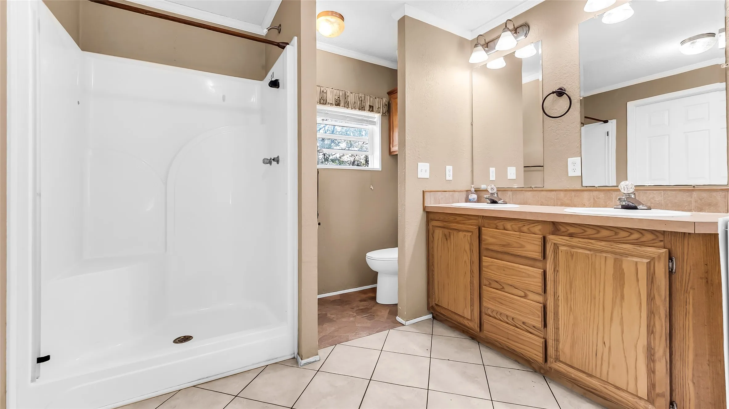 Integrated shower stall, dual vanity with wood cabinetry, large vanity mirror, and ceramic tile flooring