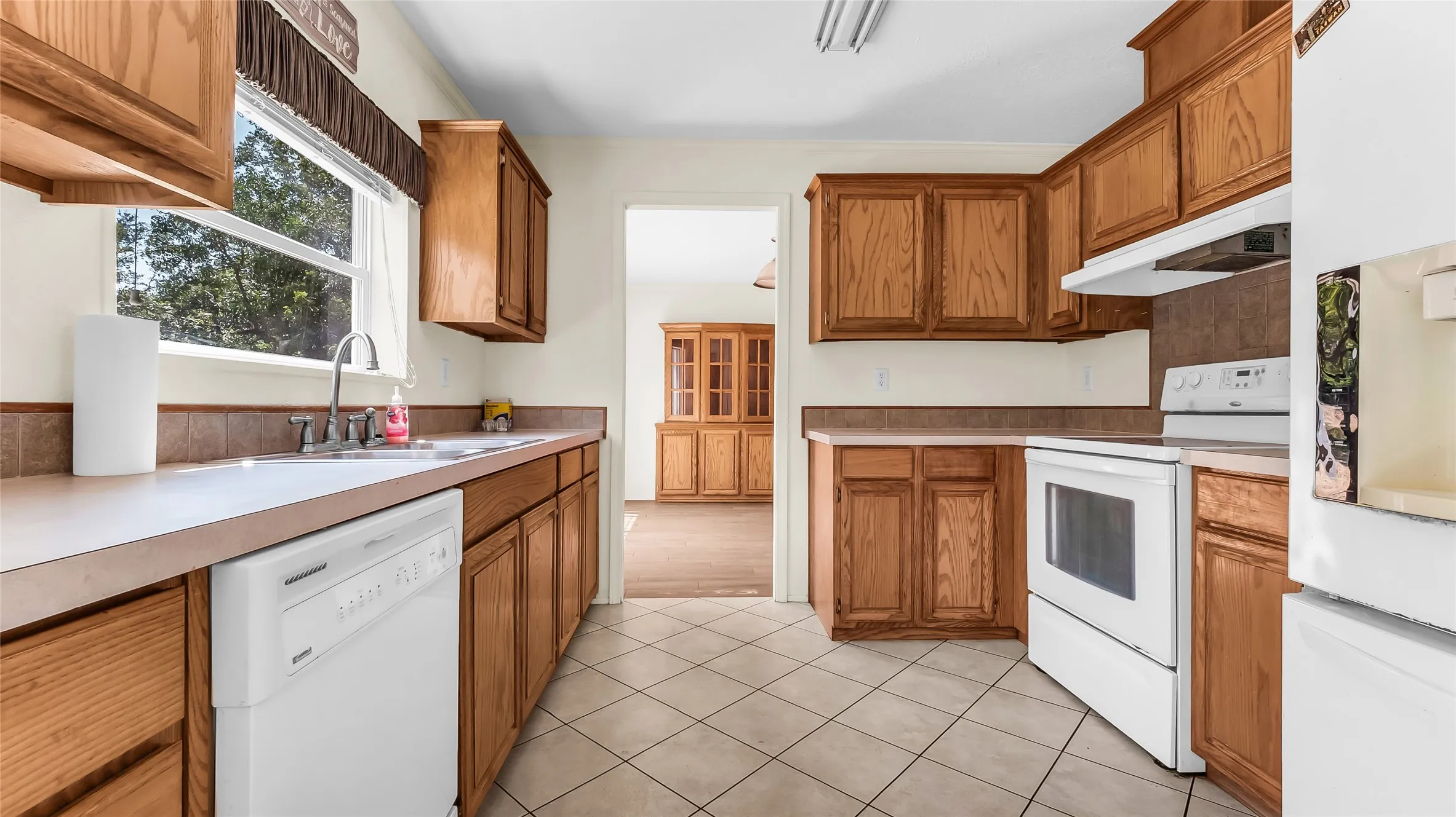 Kitchen featuring wood cabinetry, white appliances, a tile backsplash, and tile flooring
