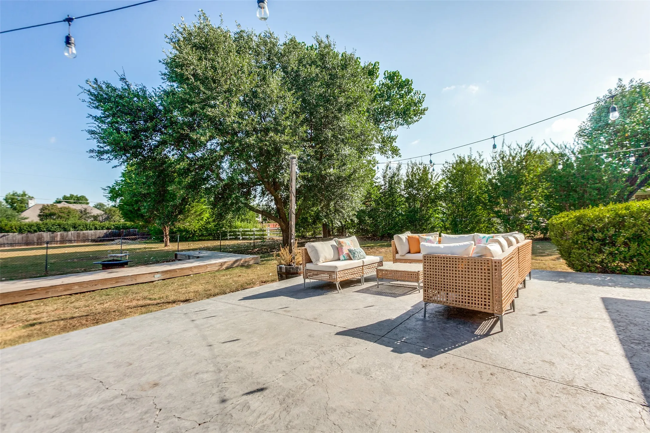Concrete patio with string lighting and a wood-lined shuffleboard court