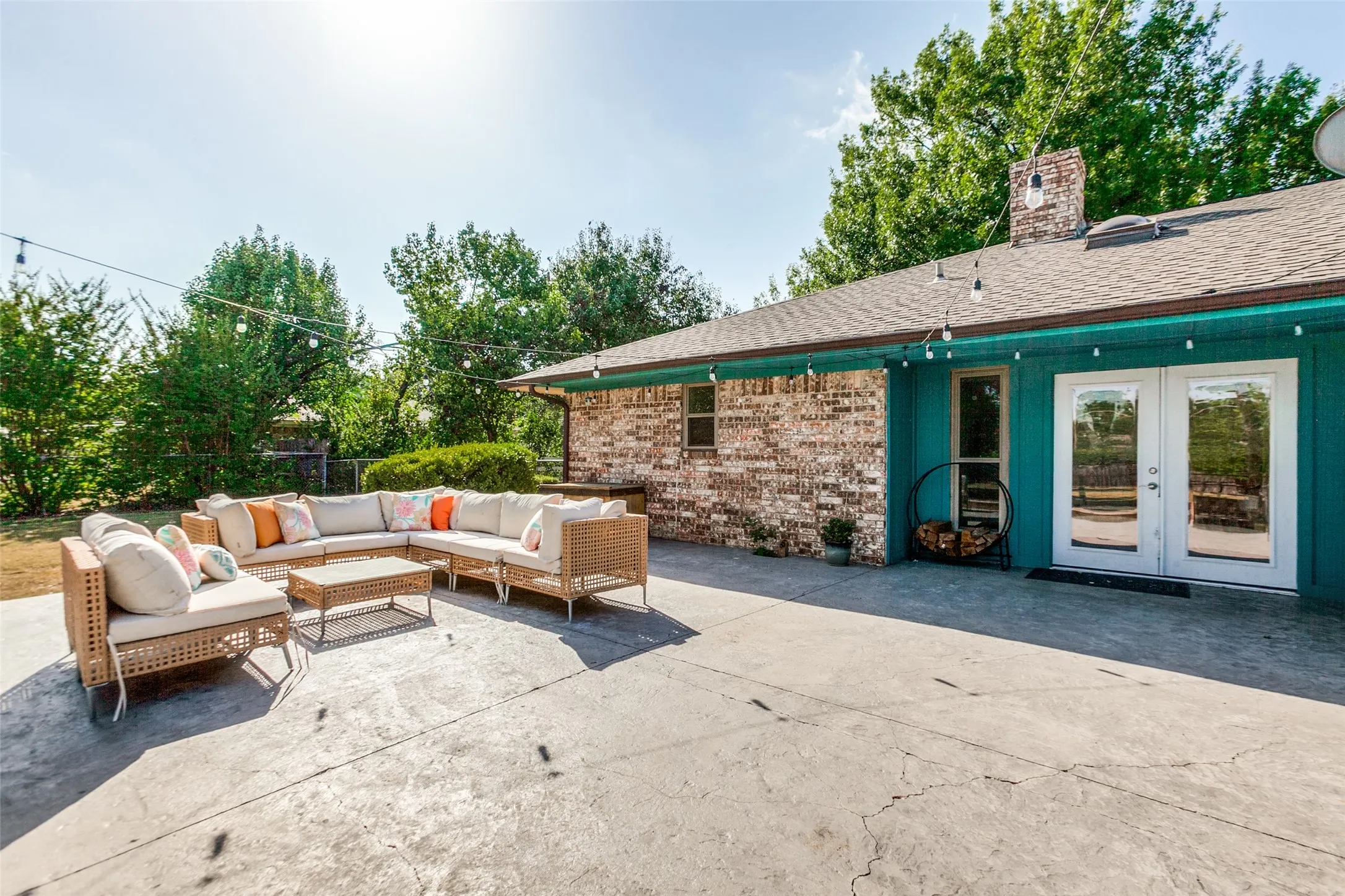 Expansive concrete patio with string lighting, brick exterior, and French doors