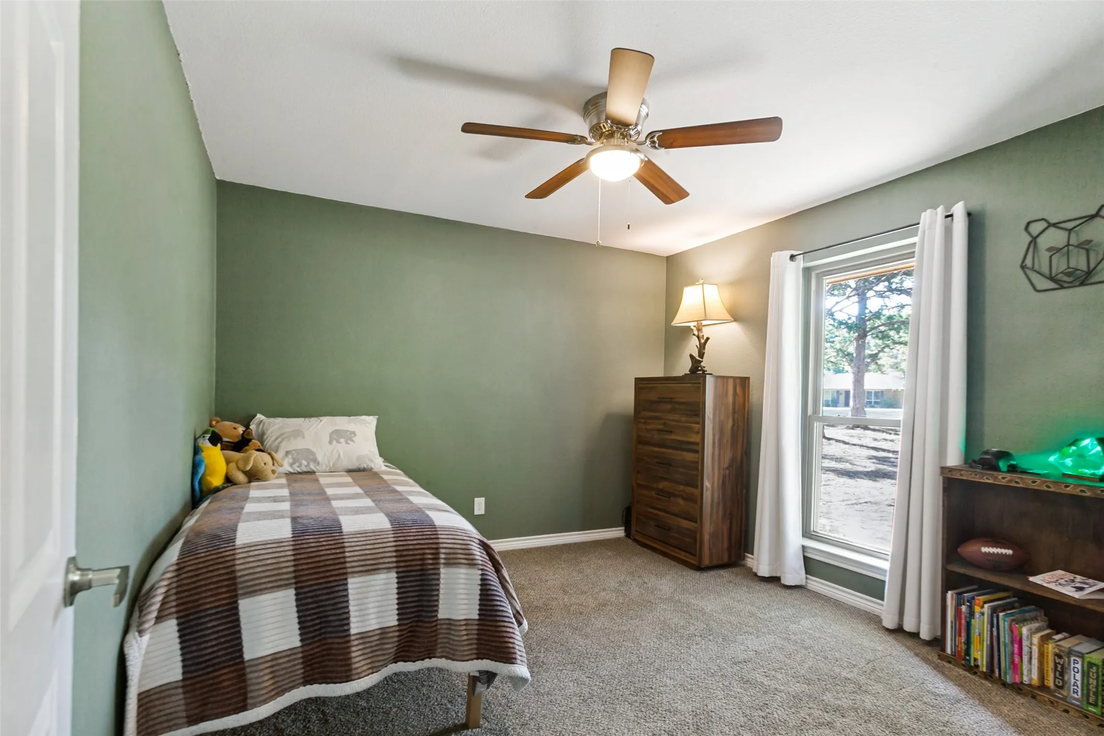 Bright secondary bedroom featuring soft sage-green walls, carpet flooring, ceiling fan with light fixture, and glass sliding door access to outdoor space