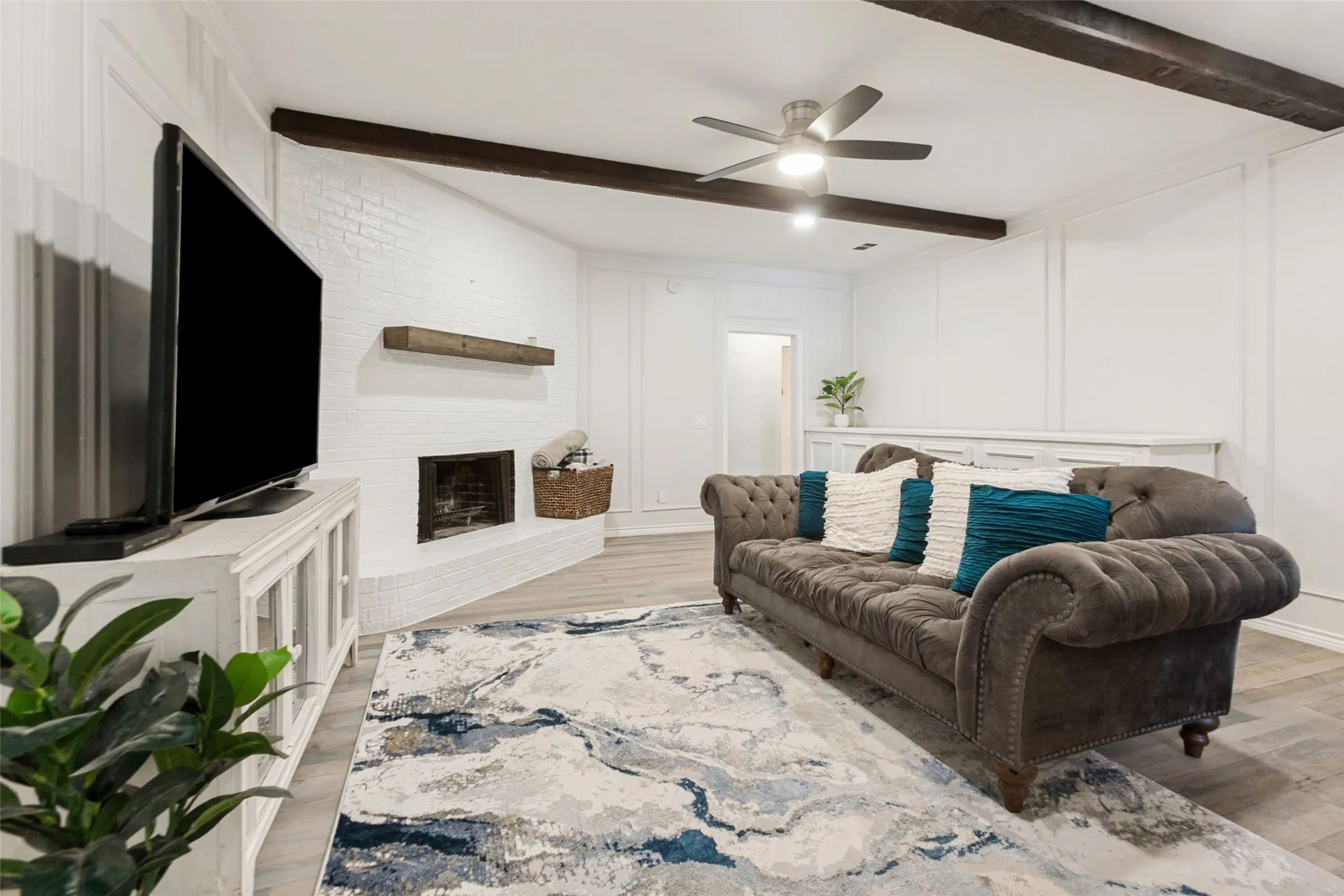 White brick fireplace with a wood mantel, wood-finish flooring, and exposed ceiling beams