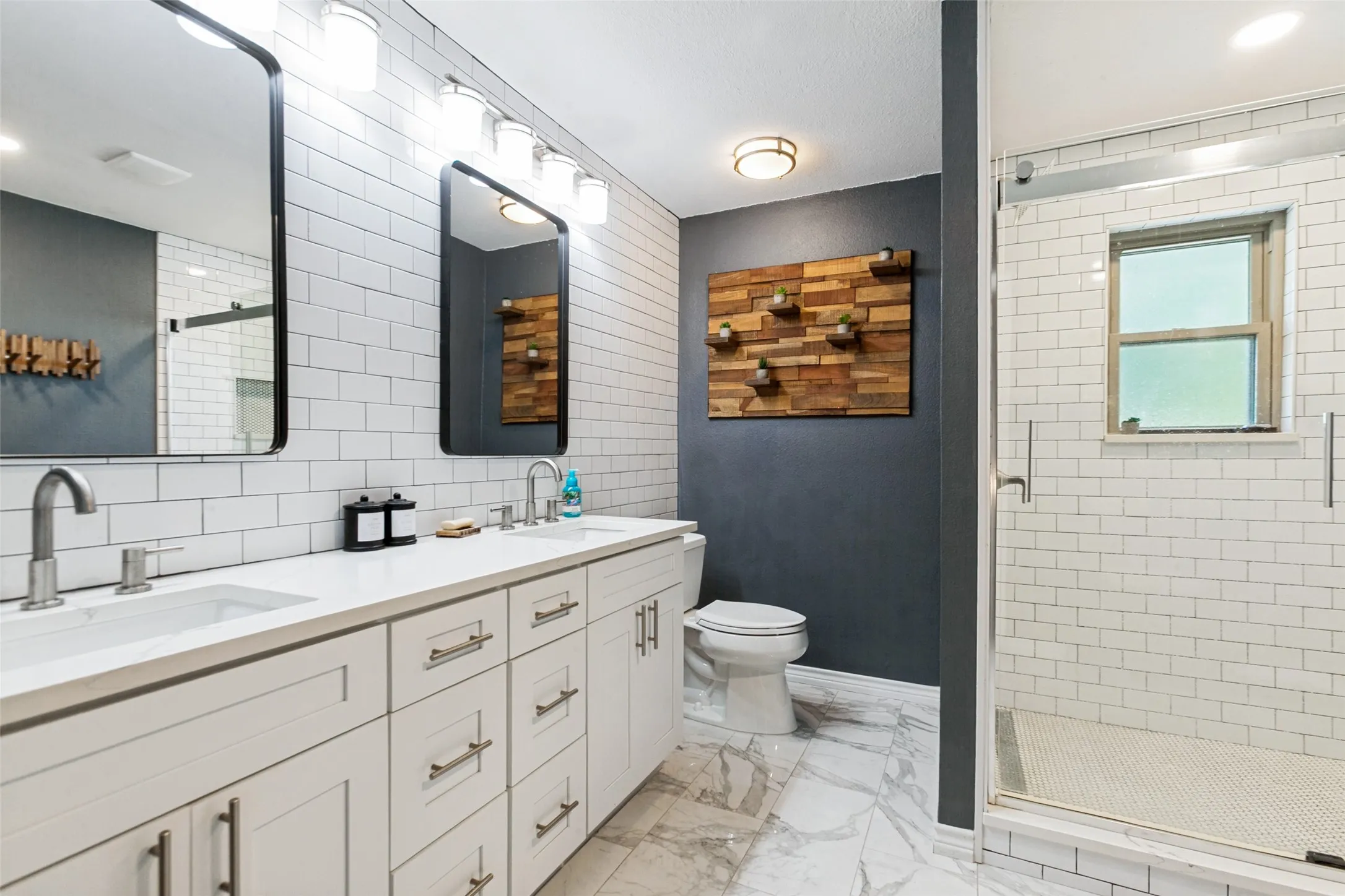 Dual vanity with white shaker-style cabinetry, undermount sinks, and contemporary wall-mounted lighting