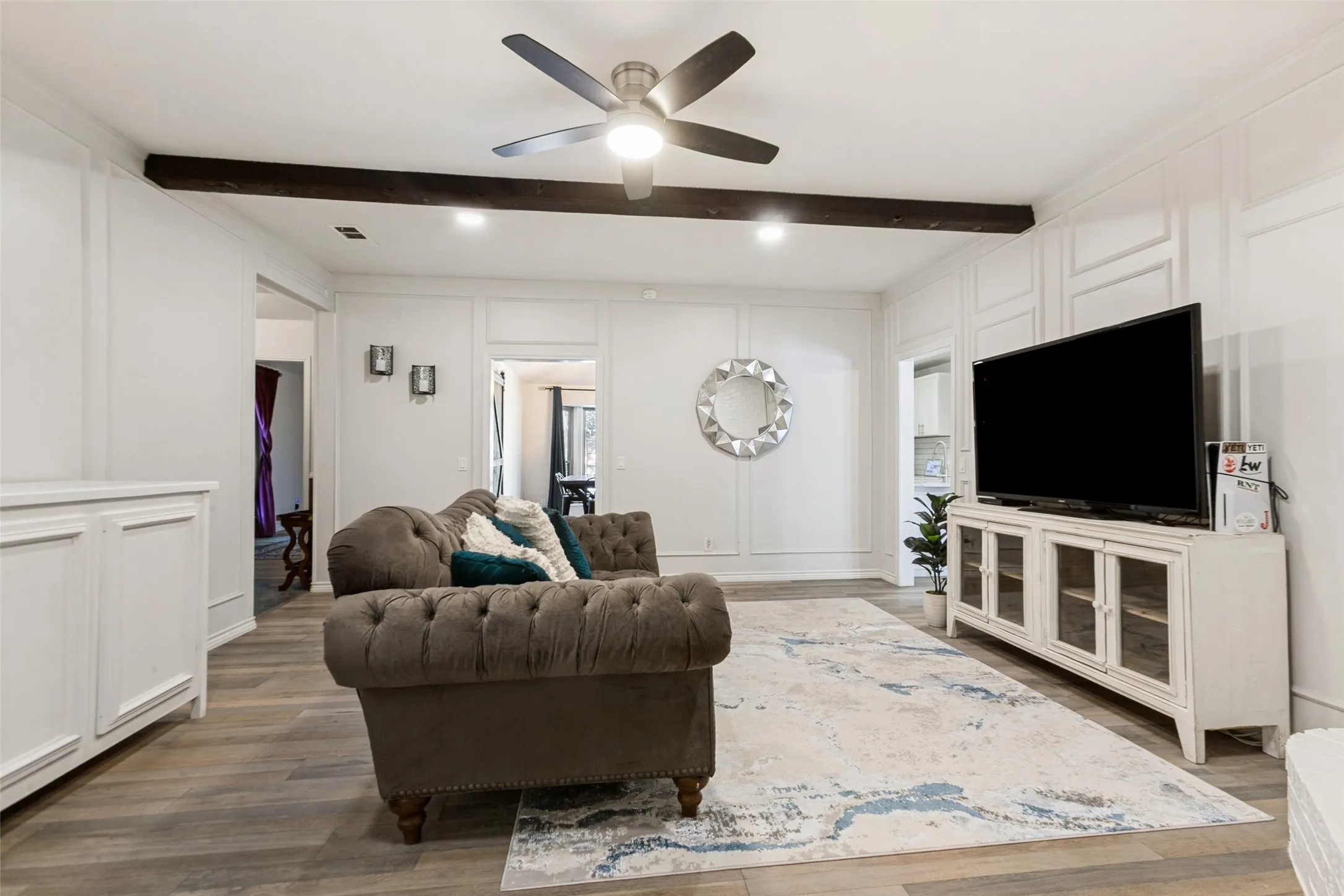 Recessed lighting, wood-finish flooring, accent wall paneling, ceiling fan, and exposed ceiling beam