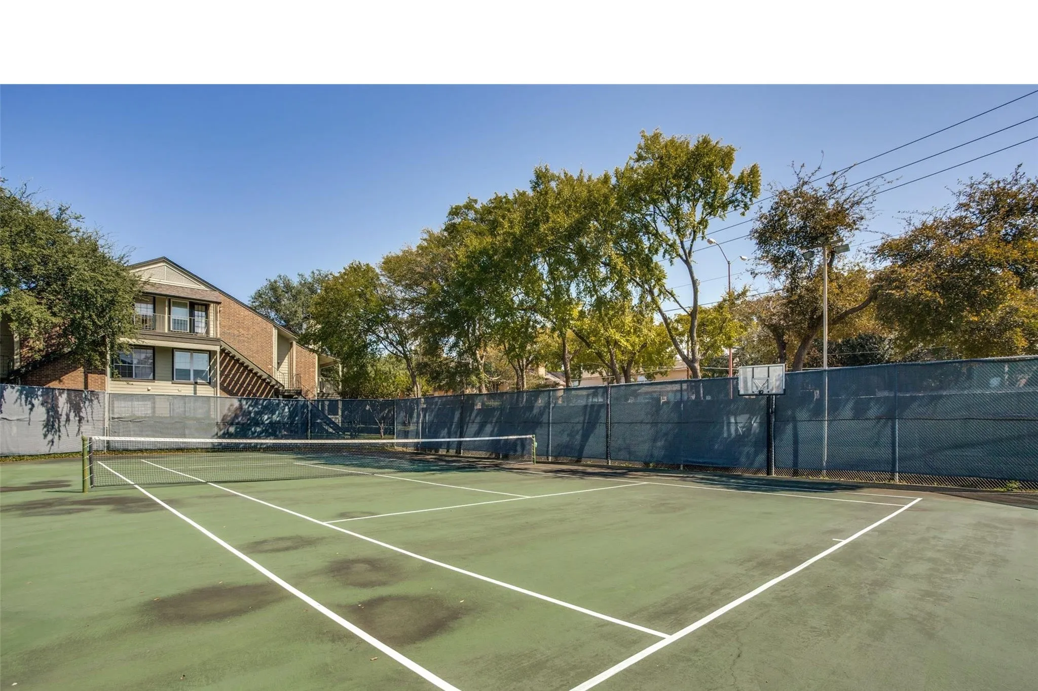 Tennis court with asphalt surface, perimeter fencing, and a basketball hoop