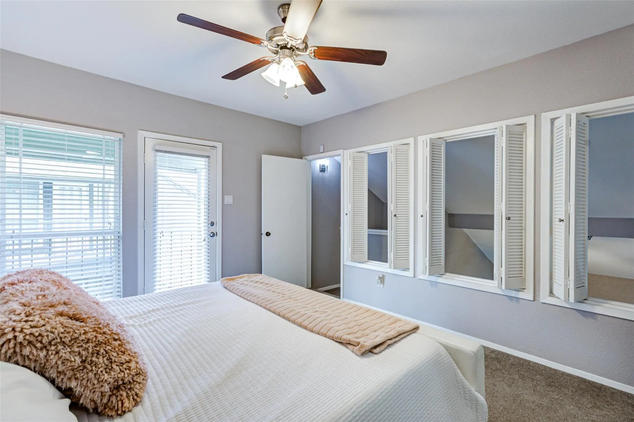 Ceiling fan with light fixture, multiple windows with blinds, built-in shuttered windows, and a glass-paneled door