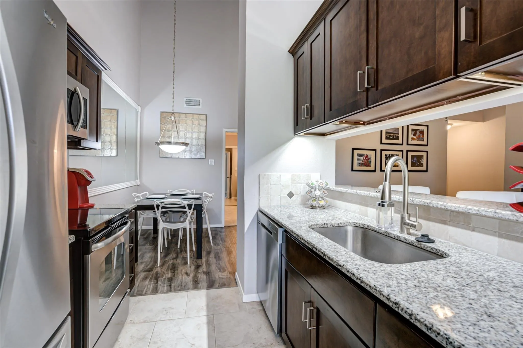 Kitchen featuring stainless steel appliances, dark wood cabinetry, granite countertops, and a tile backsplash