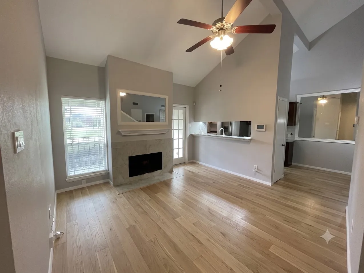 Vaulted ceilings, wood-finish flooring, stone-clad fireplace, and a ceiling fan with integrated lighting
