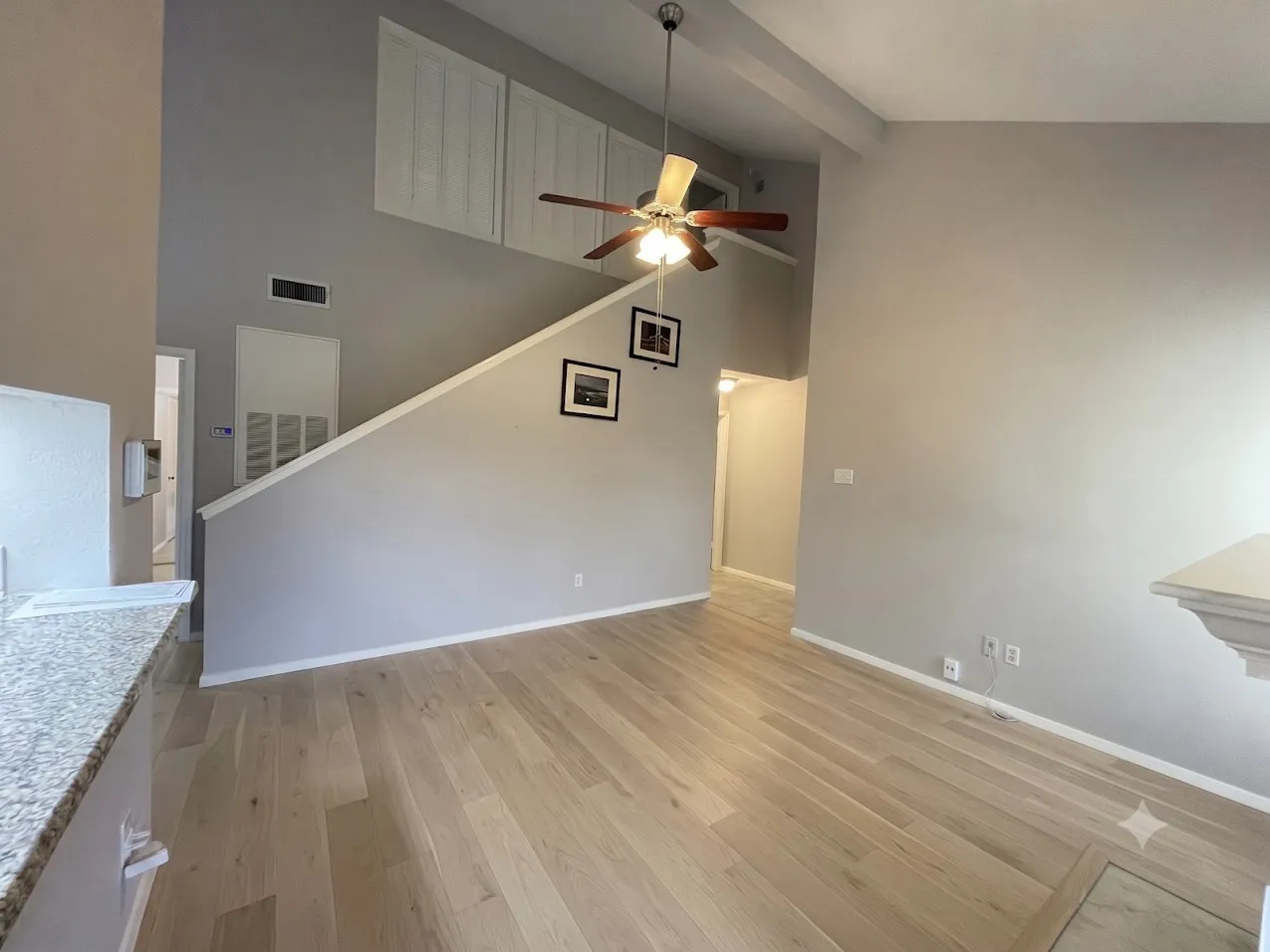 Vaulted ceiling, ceiling fan with light fixture, wood-finish flooring, two-tone wall paint, and granite-finish countertop