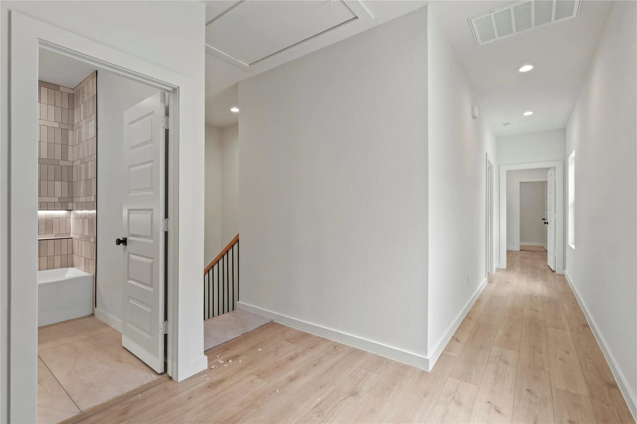 Recessed lighting, wood-finish flooring, white paneled doors, black door hardware, and a staircase with black iron balusters