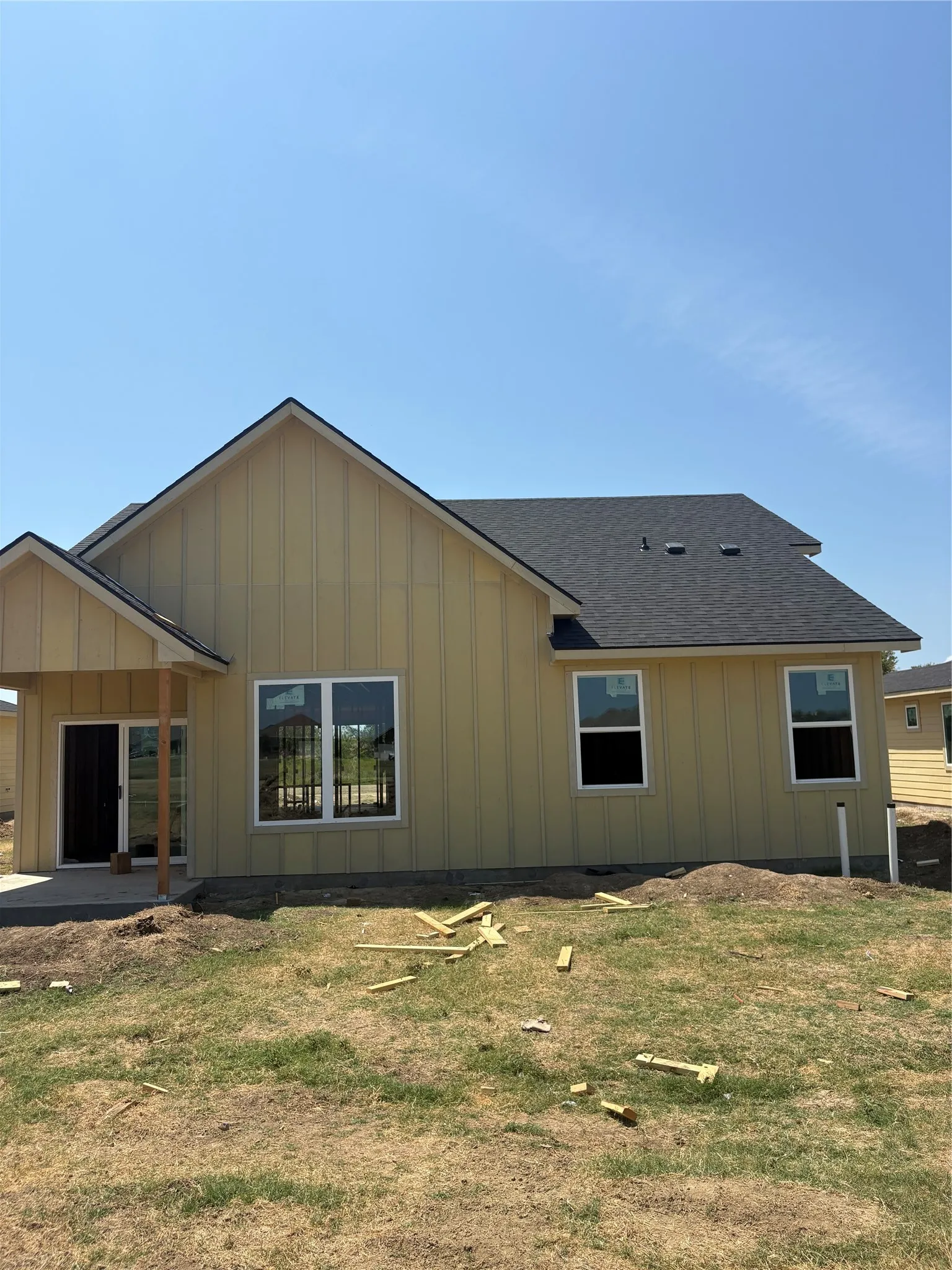 Light yellow siding exterior with a dark shingle roof, featuring multiple large windows and a covered patio area