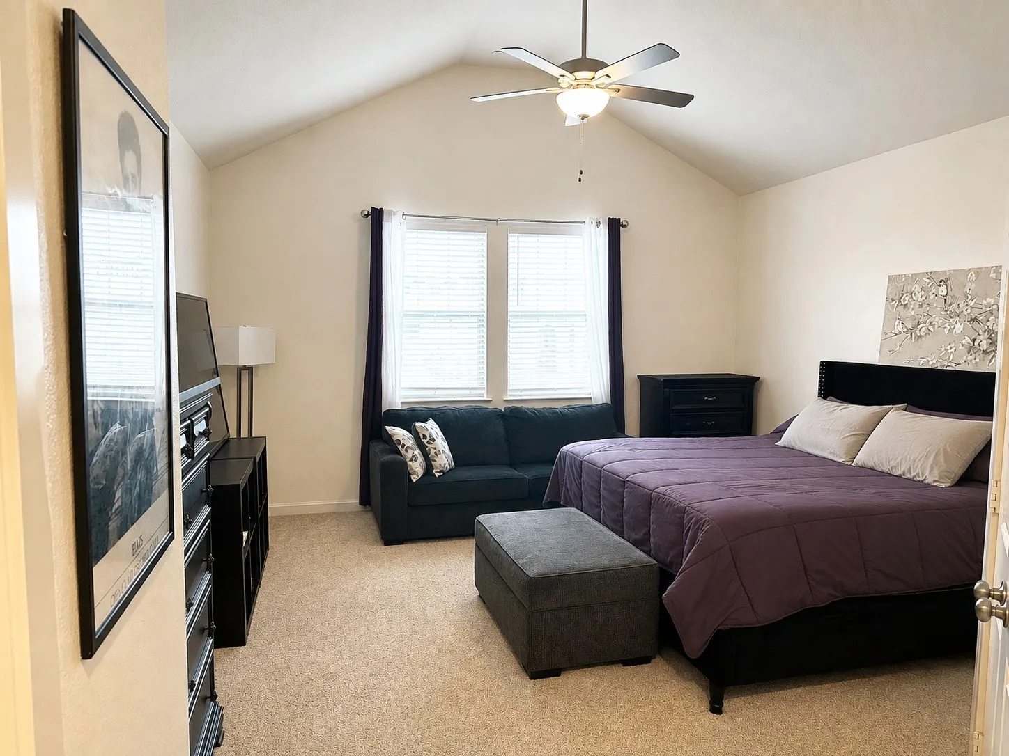 Primary Bedroom: Vaulted ceiling with a ceiling fan, neutral wall paint, carpet flooring, and a large window with blinds. Digitally declutterred.
