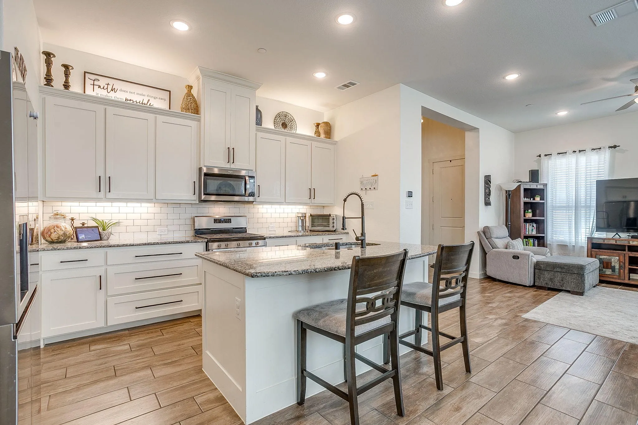 Open kitchen featuring white cabinetry, subway tile backsplash, stainless steel appliances, granite countertops, and wood-finish flooring