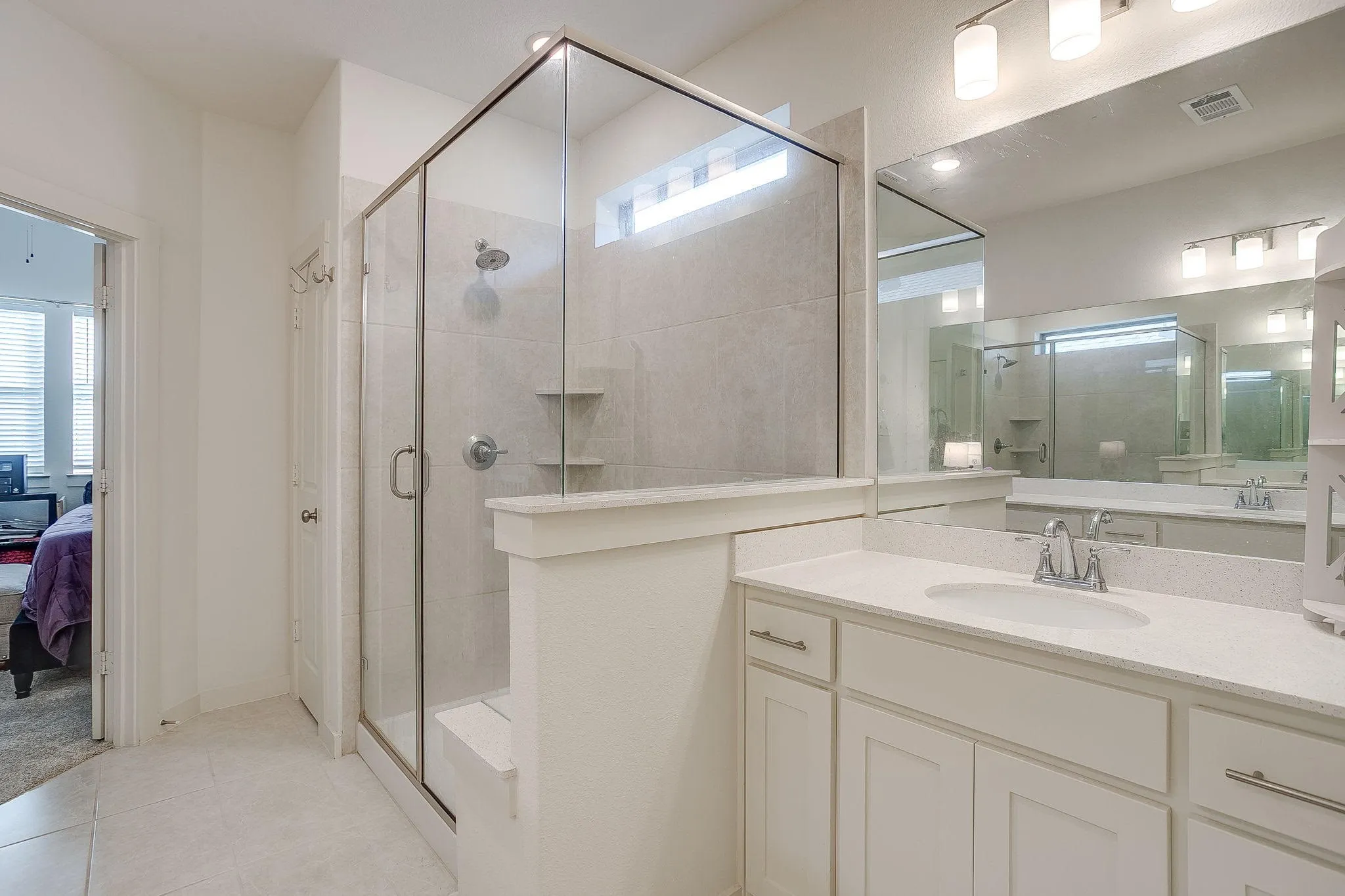 Primary Bathroom: Glass-enclosed shower with a built-in bench and recessed shelving, white vanity with an integrated sink and light-colored countertop, and a large wall-mounted mirror