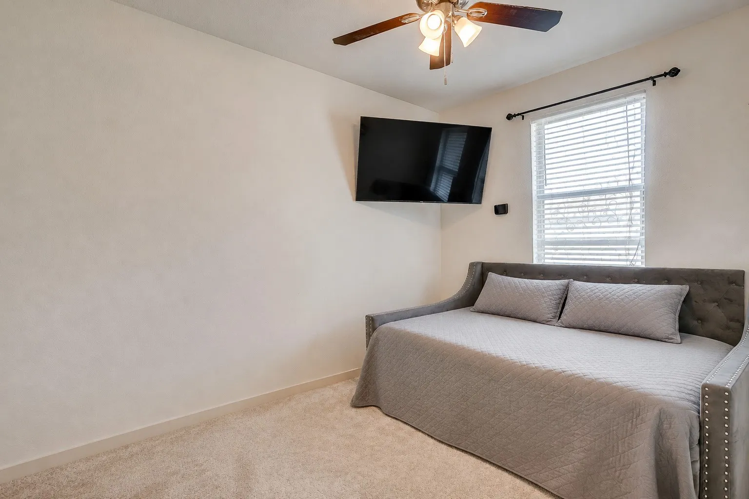 Bedroom: Neutral paint palette with carpet flooring, a ceiling fan with integrated lighting, and window blinds. Digitally declutterd.