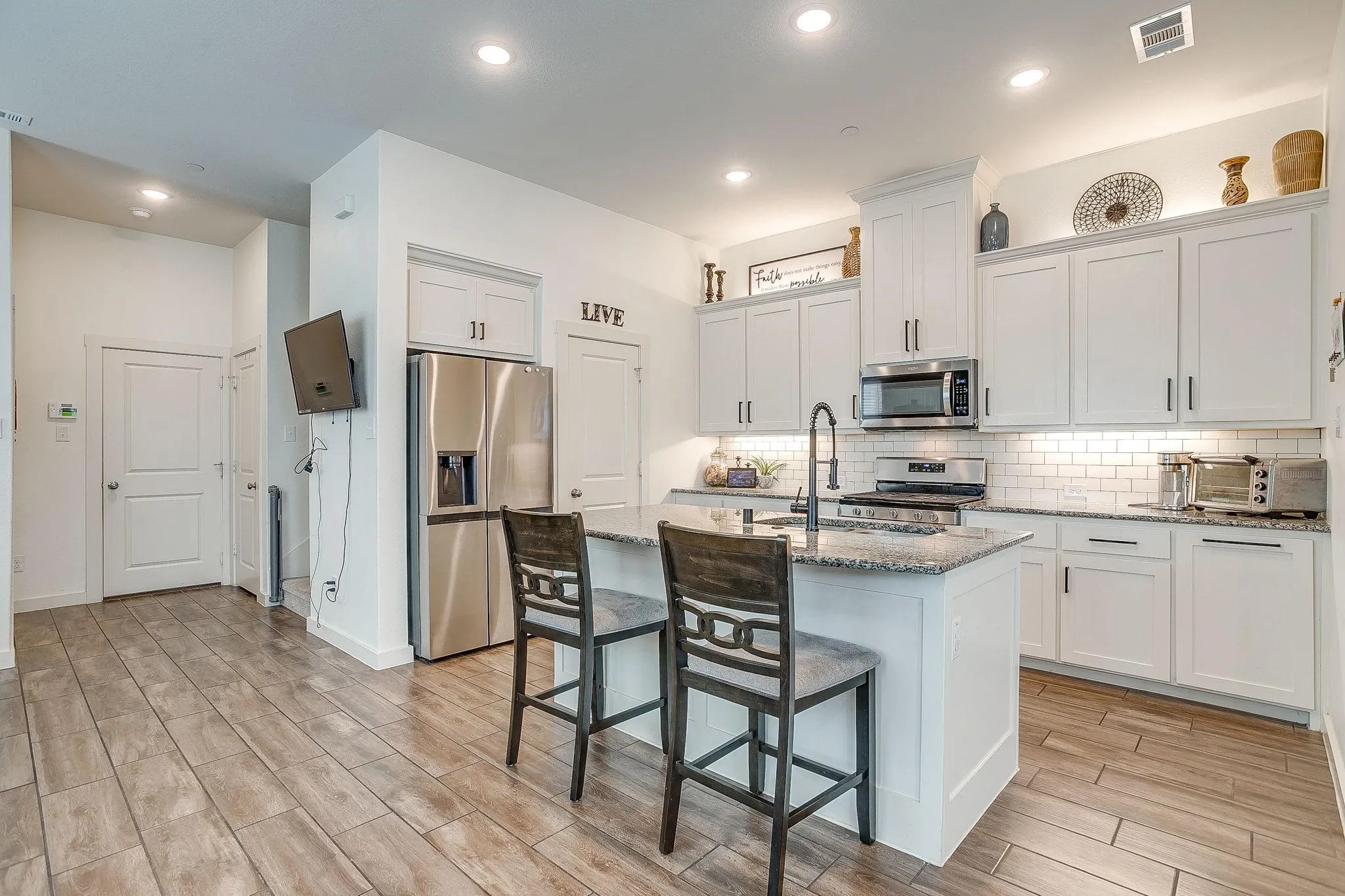 Kitchen featuring a central island with a granite countertop, white shaker-style cabinetry, stainless steel appliances, a white subway tile backsplash, and wood-finish flooring